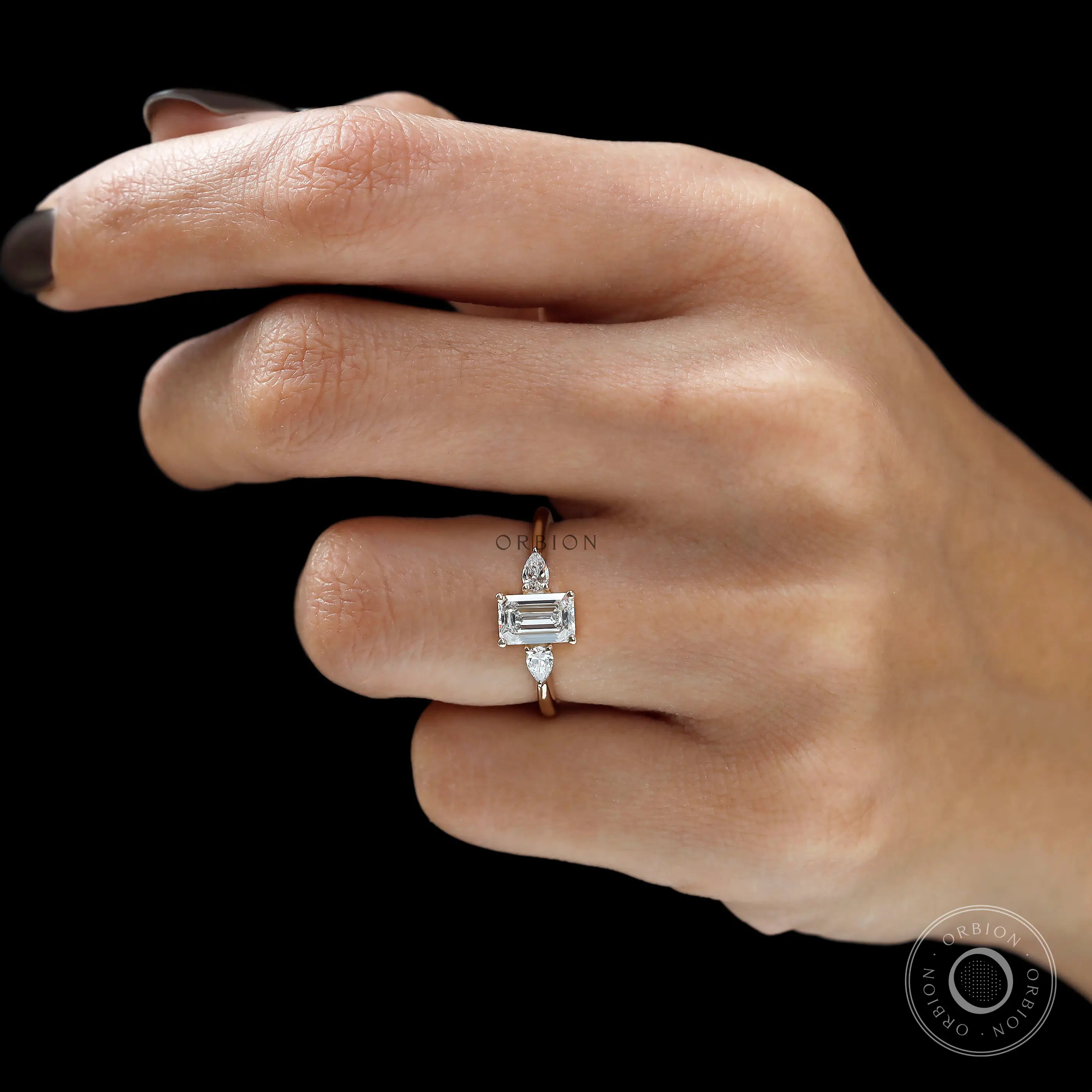 Emerald cut engagement ring with pear side stones on finger