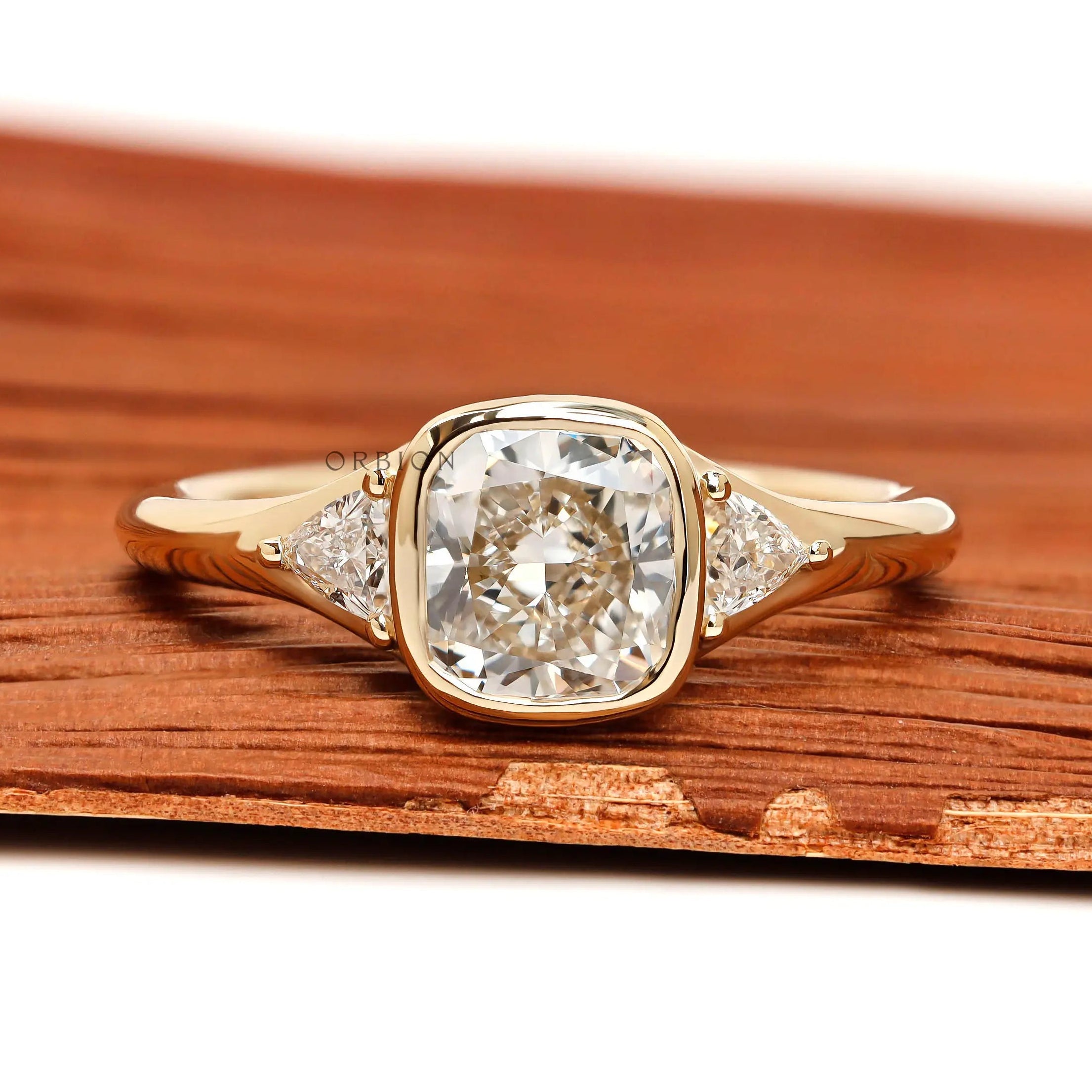 Floating three stone cushion bezel engagement ring with trillion side stones in yellow gold