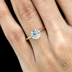 Elongated round solitaire engagement ring in 14K yellow gold on finger