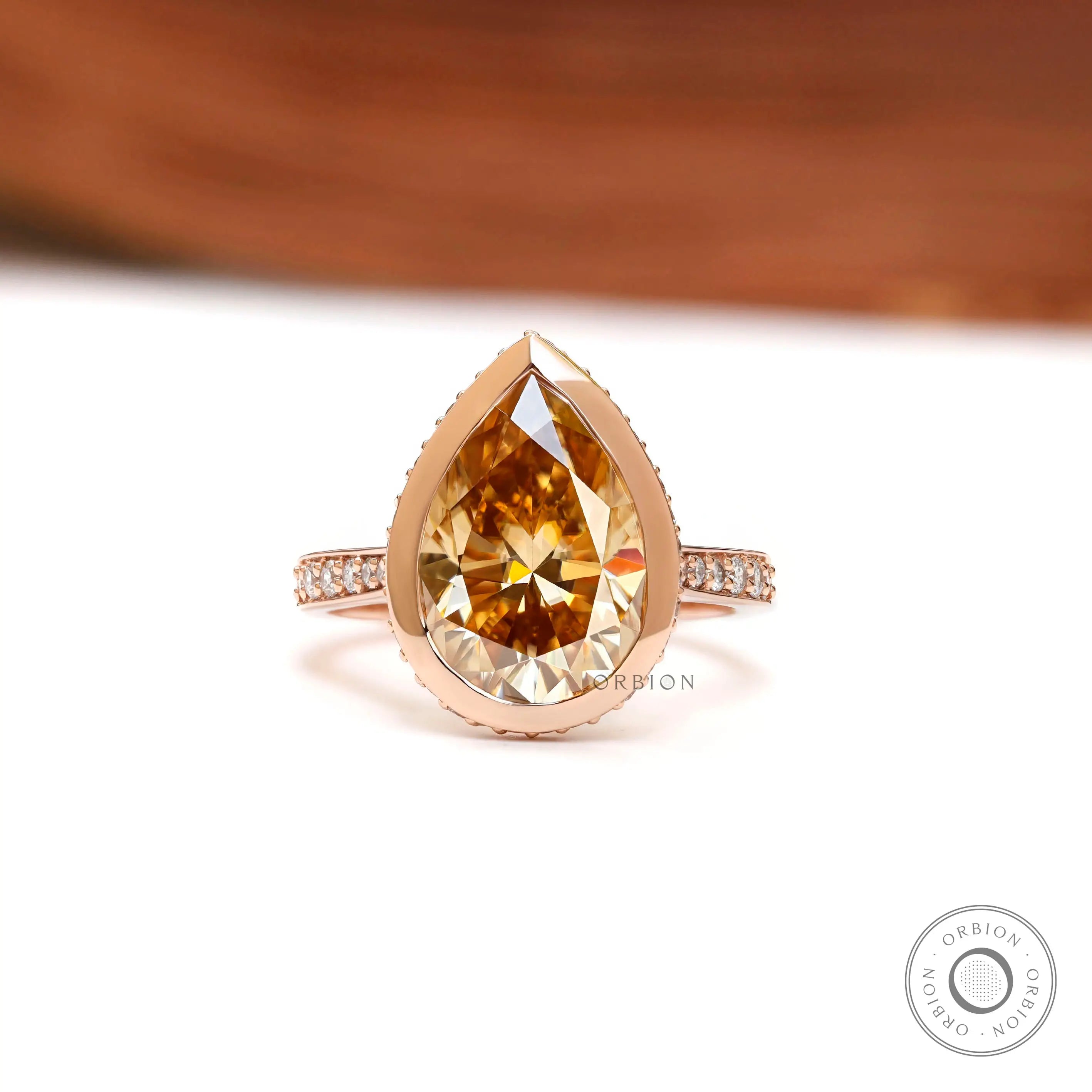 Close up of pear champagne moissanite bezel halo ring in rose gold