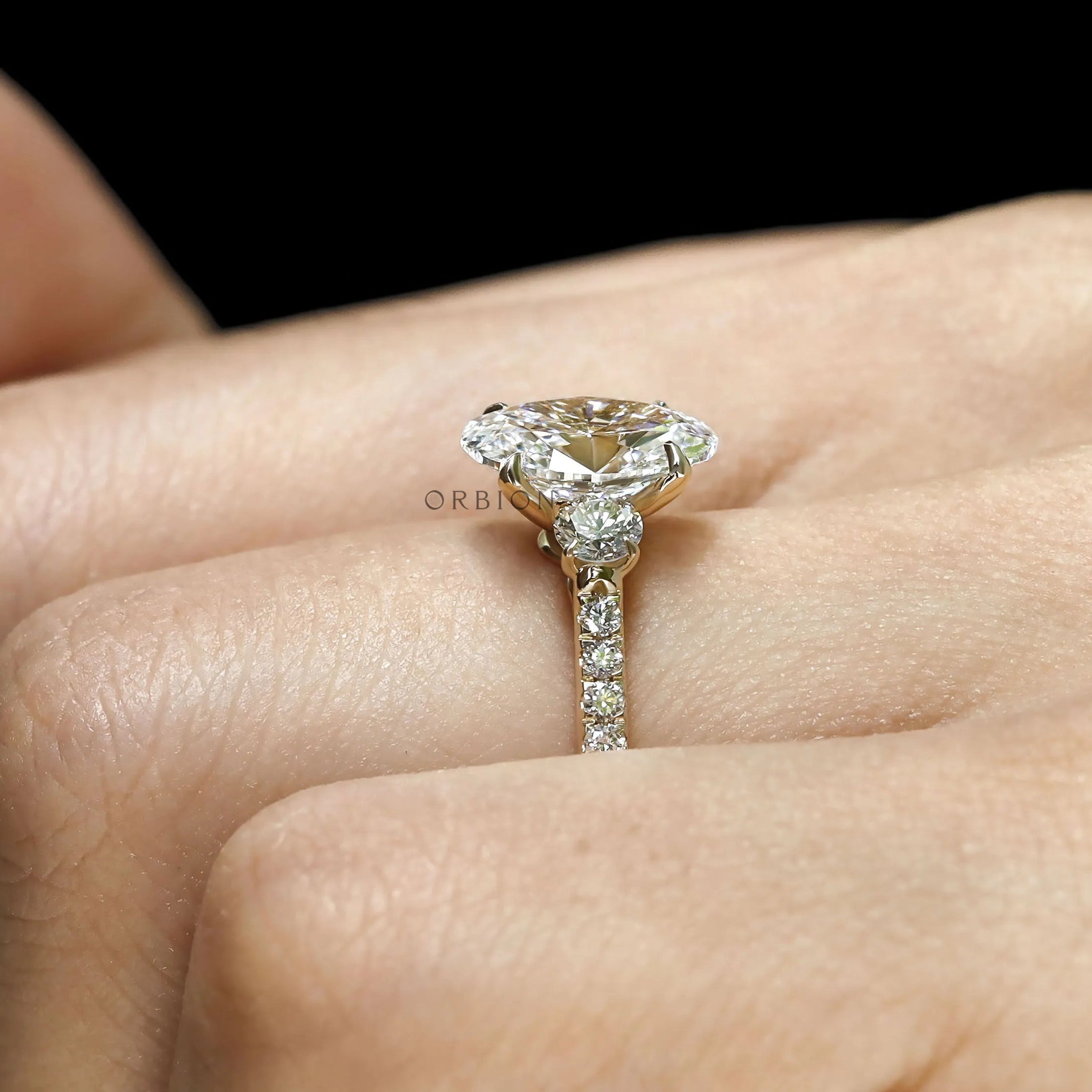 Oval lab grown diamond engagement ring with three stones, yellow gold cathedral band, pave shank