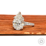 Pear shaped moissanite engagement ring with cathedral setting and pave band