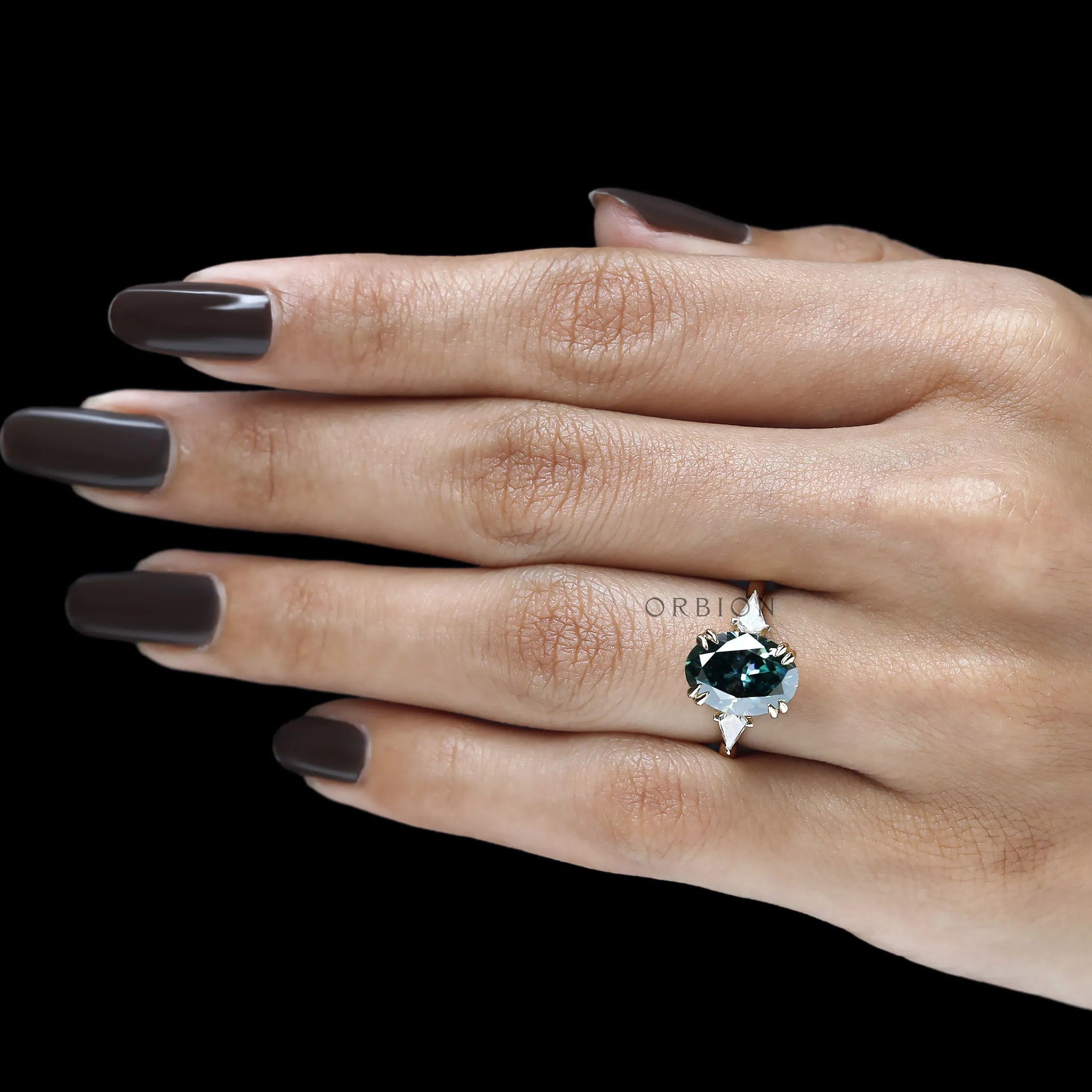 14k yellow gold trilogy ring featuring oval blue green moissanite and floral inspired bridge