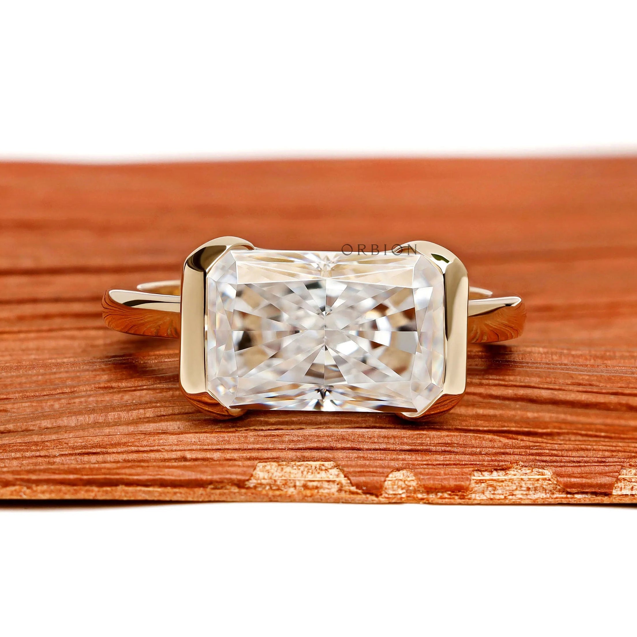 East west radiant cut moissanite or lab diamond engagement ring with sleek half bezel floating setting in 14k yellow gold
