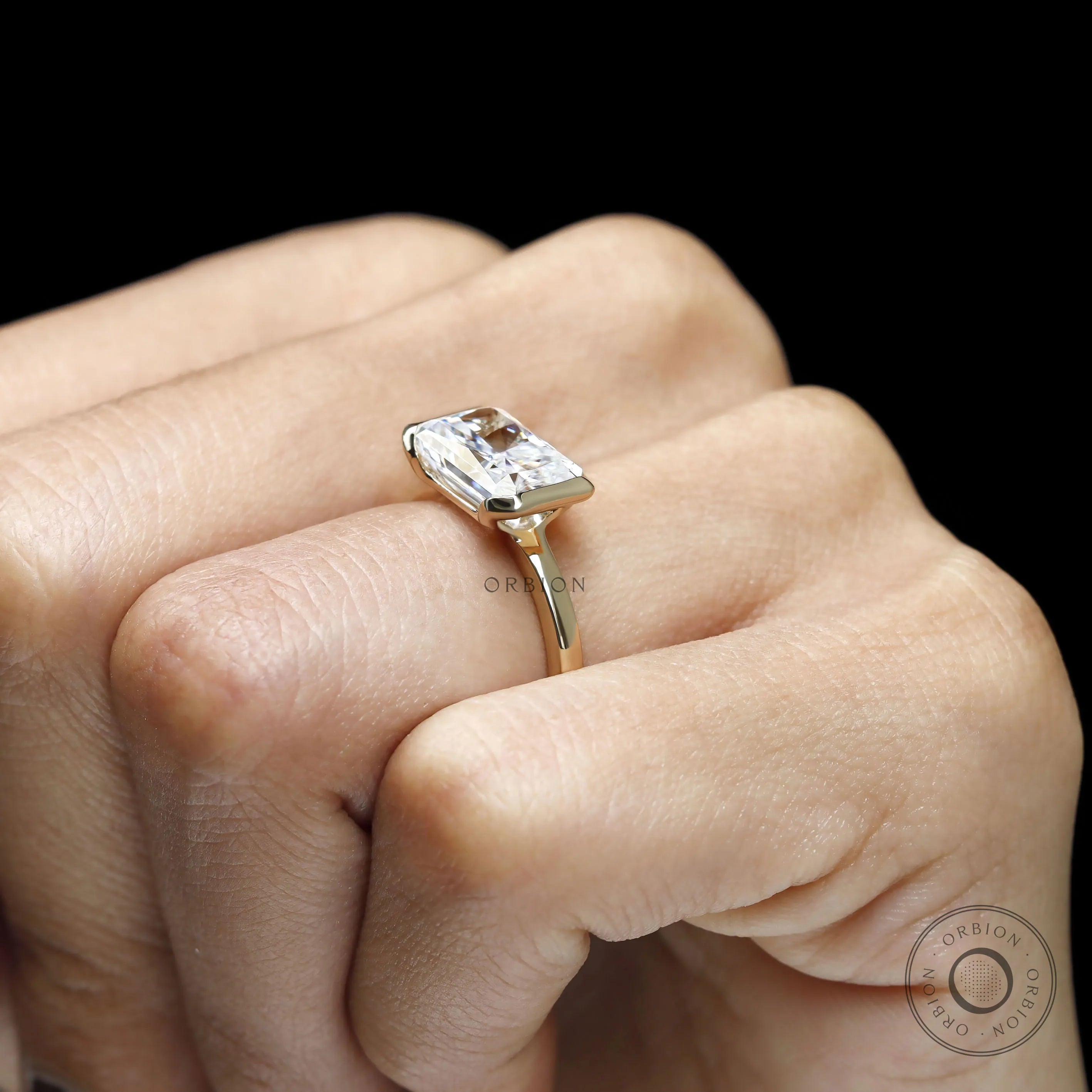 Modern fine jewelry ring with radiant cut moissanite, half bezel floating design and 14k yellow gold band