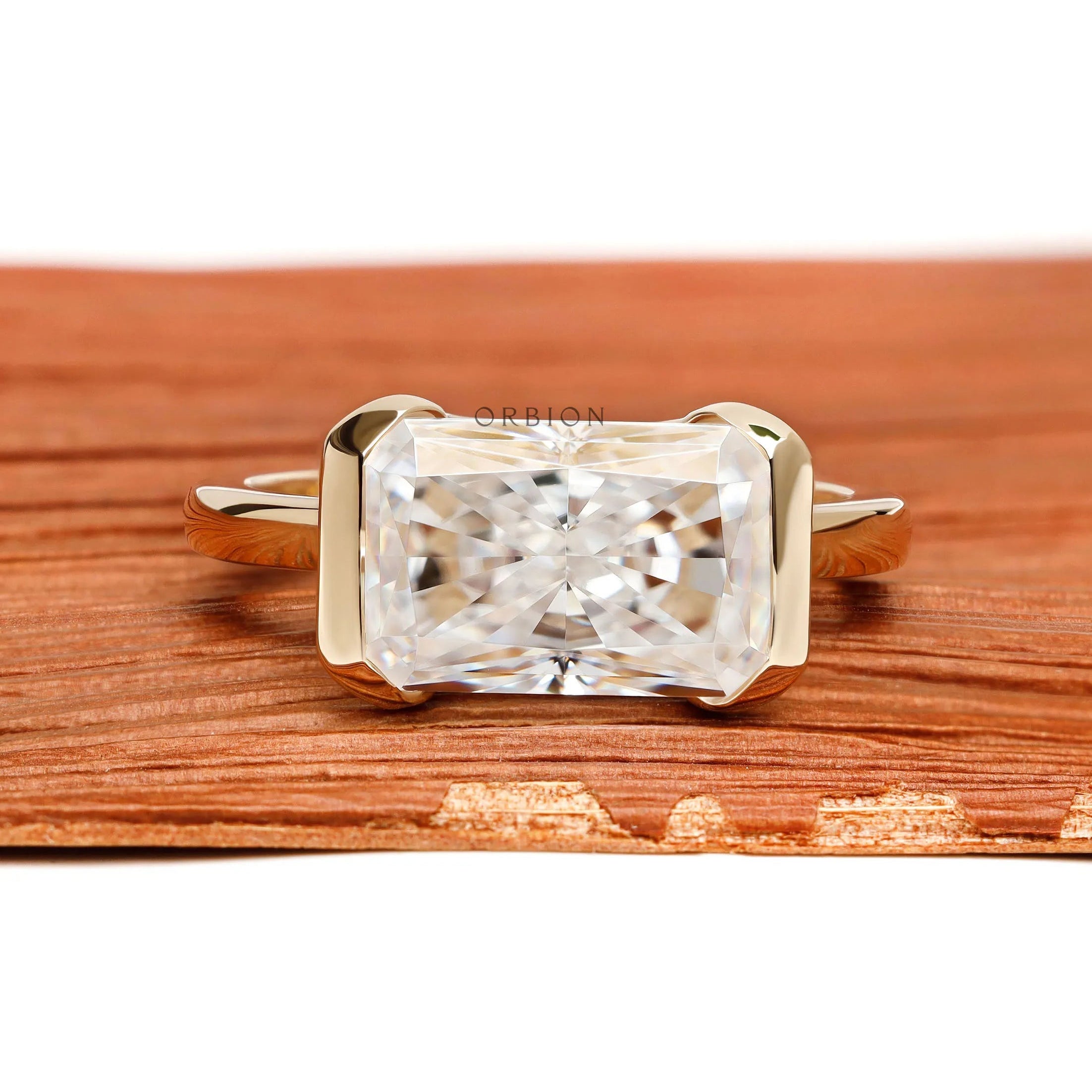 East west radiant cut moissanite or lab diamond engagement ring with sleek half bezel floating setting in 14k yellow gold