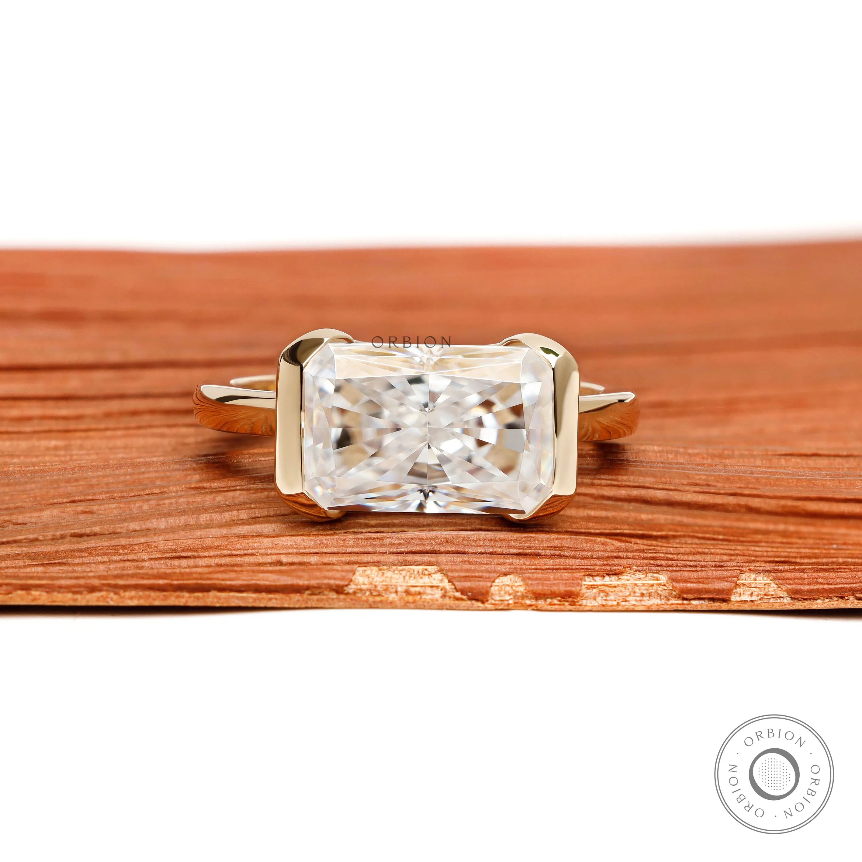 East west radiant cut moissanite or lab diamond engagement ring with sleek half bezel floating setting in 14k yellow gold