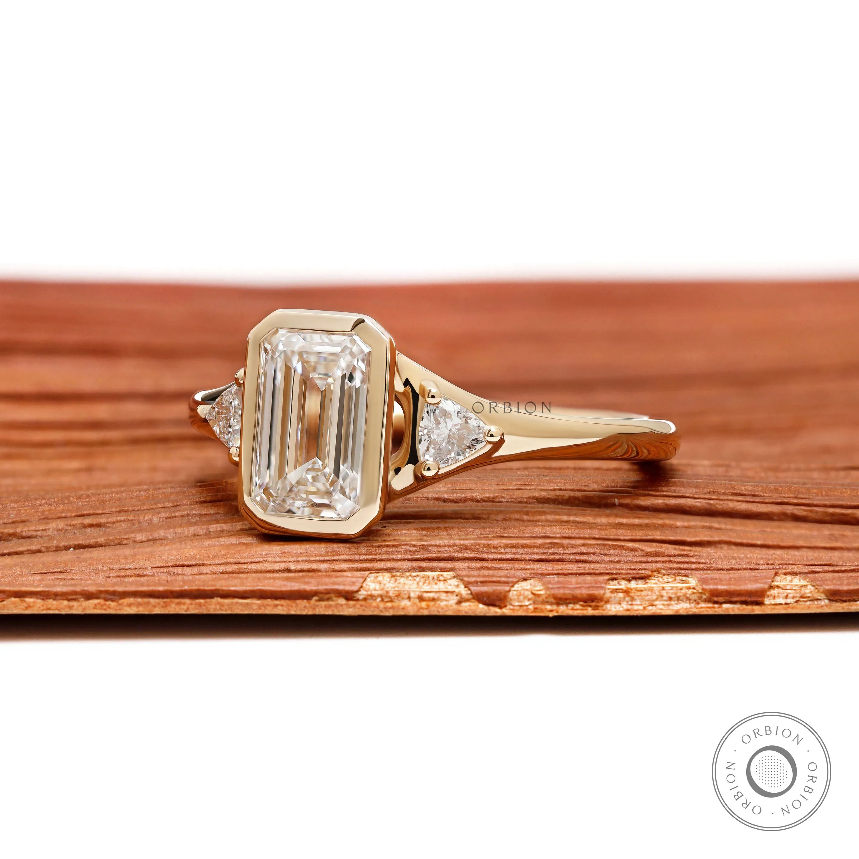 14k yellow gold emerald cut lab diamond trilogy ring featuring three stone bezel design and minimalist wedding style