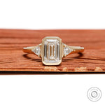 Emerald cut three stone engagement ring with lab grown diamond or moissanite trilogy bezel setting in 14k yellow gold