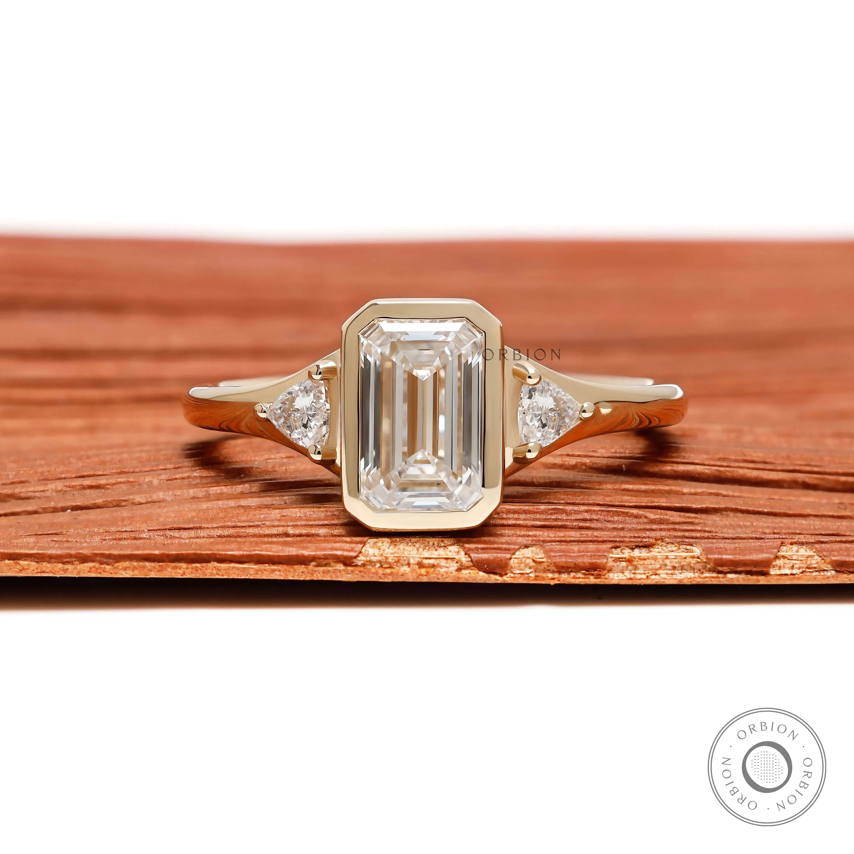 Emerald cut three stone engagement ring with lab grown diamond or moissanite trilogy bezel setting in 14k yellow gold