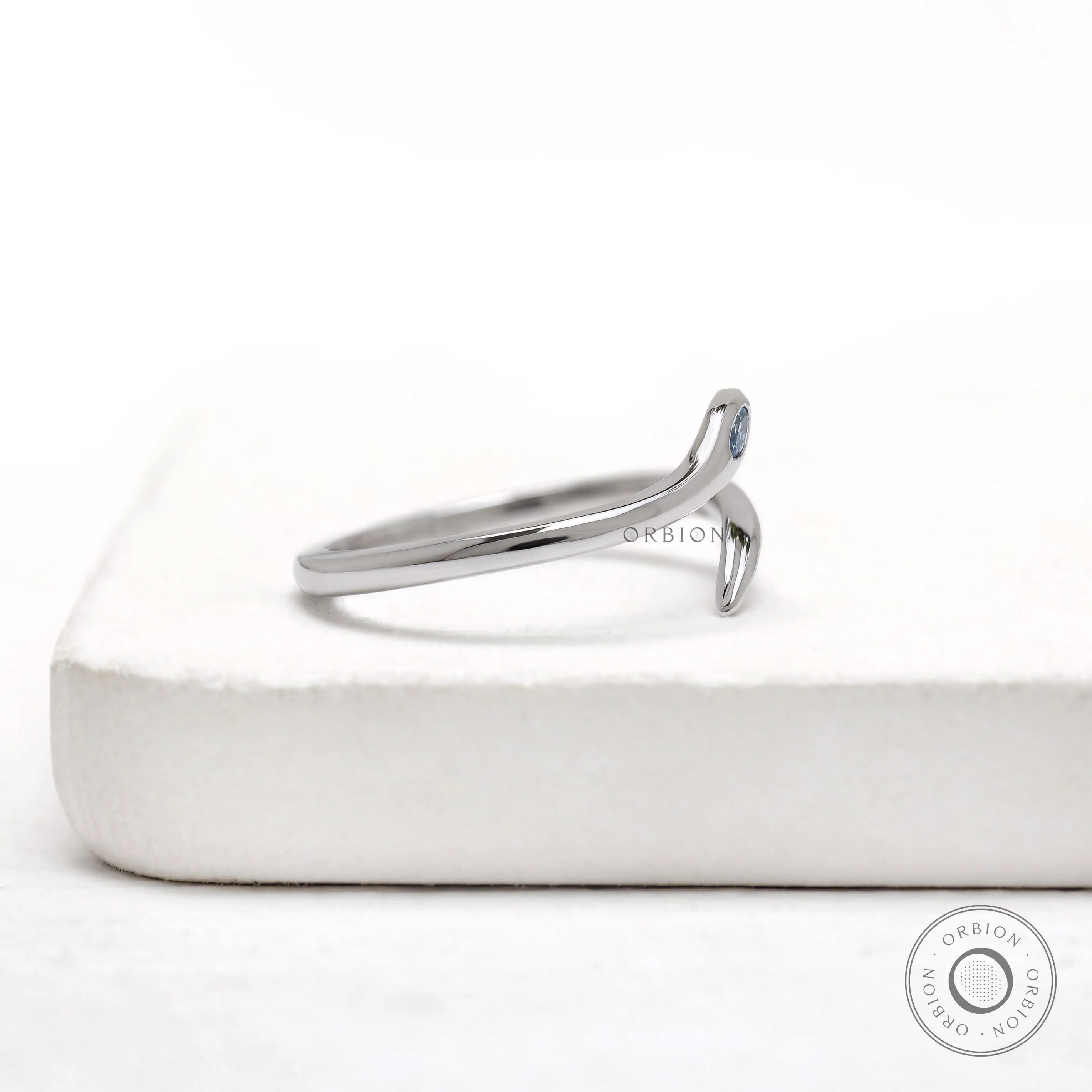 White gold open wrap snake ring featuring a flush set blue diamond