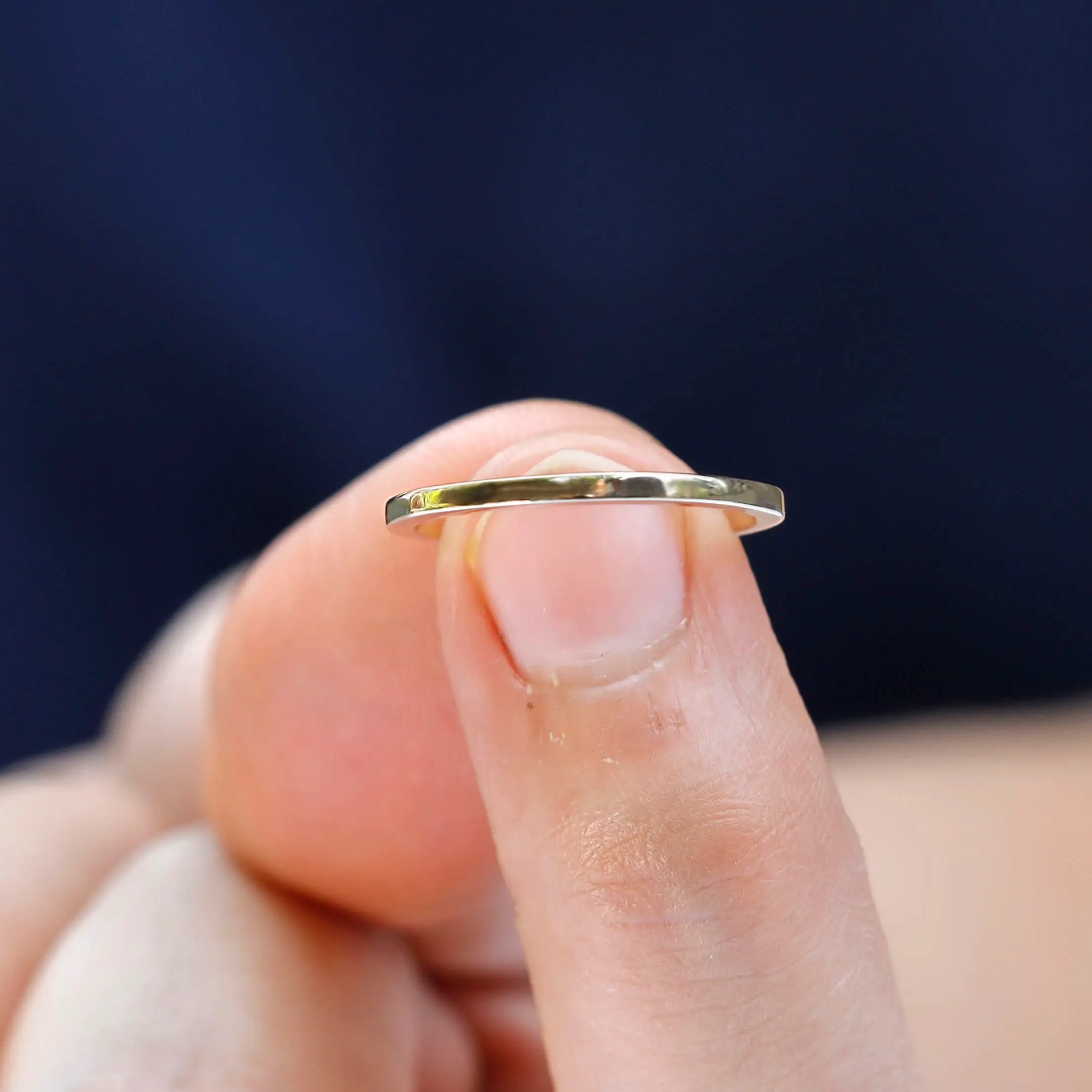 Minimal gold band held on fingertip showing slim width and smooth finish