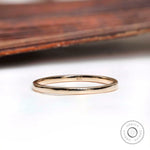 Thin minimalist gold wedding band resting on a white surface with a wooden background