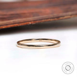 Thin minimalist gold wedding band resting on a white surface with a wooden background