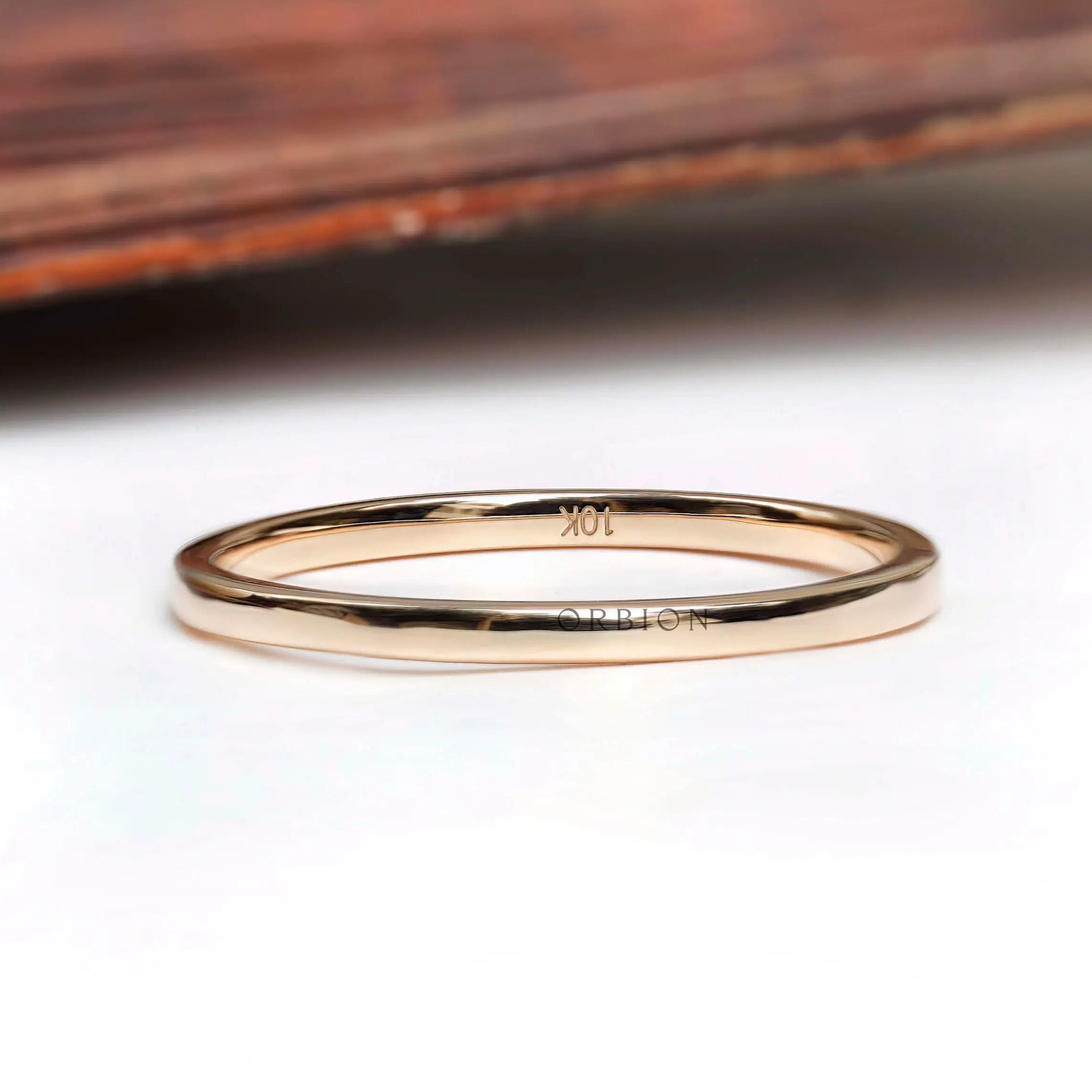 Thin minimalist gold wedding band resting on a white surface with a wooden background