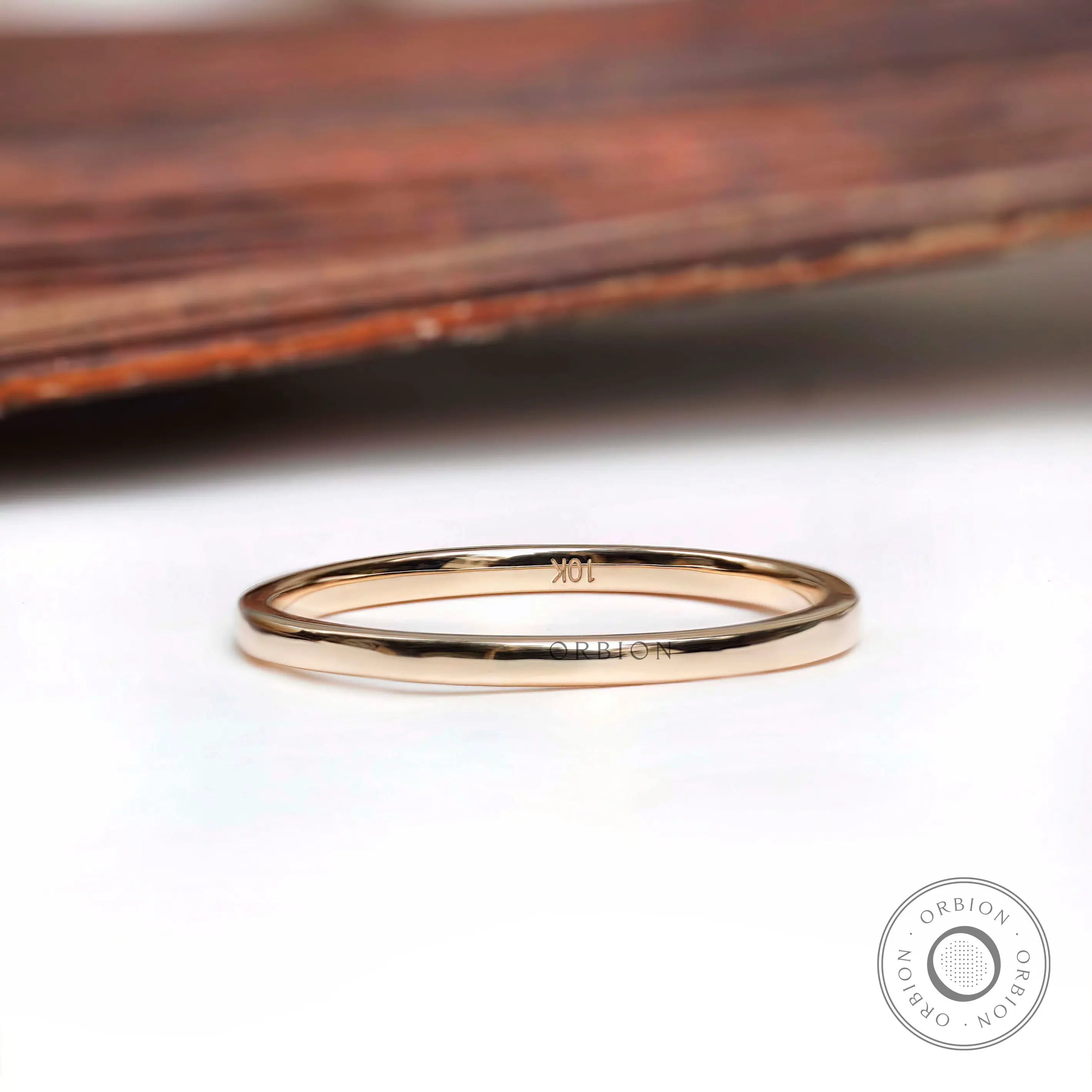 Thin minimalist gold wedding band resting on a white surface with a wooden background