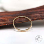 Dainty solid gold stacking ring displayed upright against a rustic wood backdrop