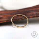 Dainty solid gold stacking ring displayed upright against a rustic wood backdrop