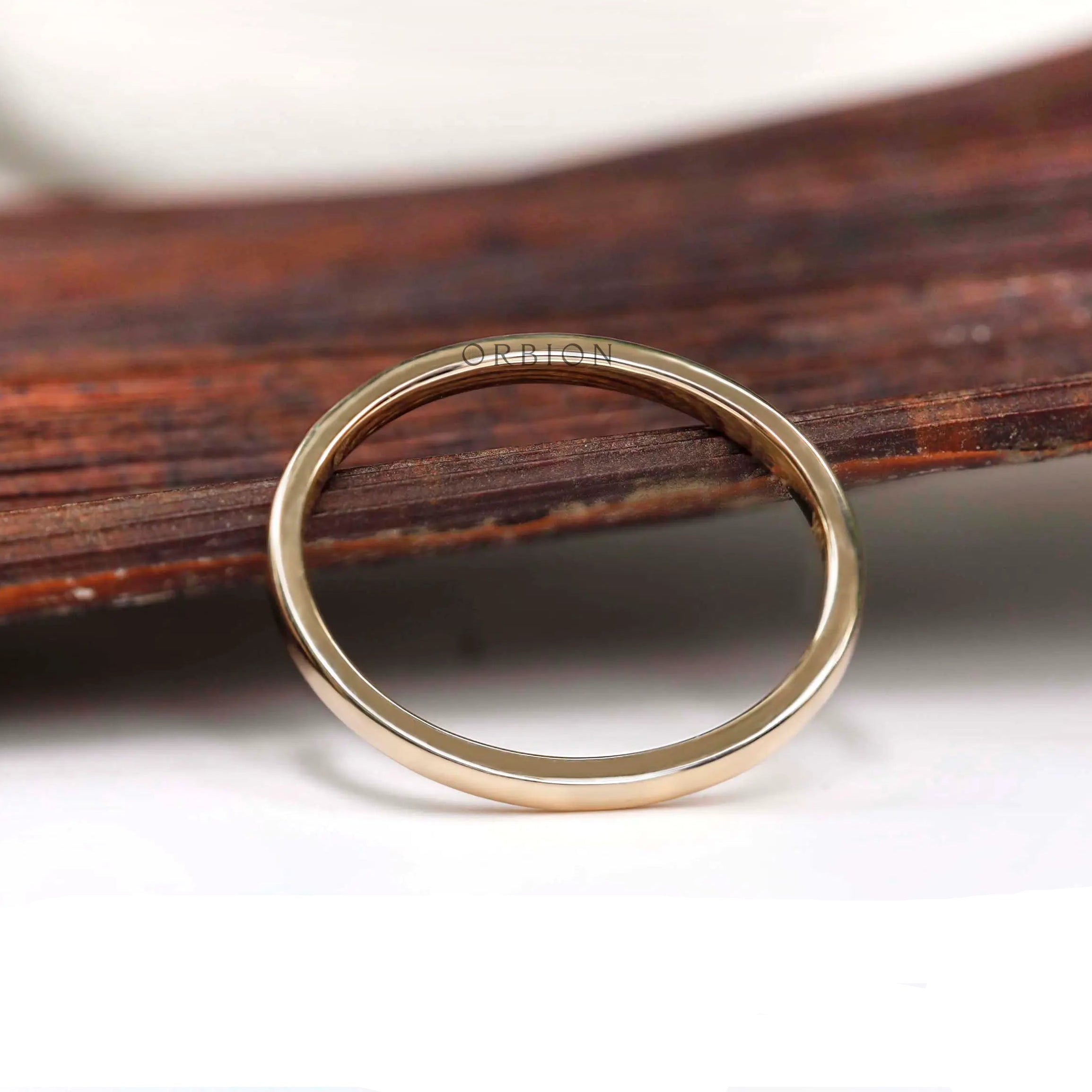 Dainty solid gold stacking ring displayed upright against a rustic wood backdrop