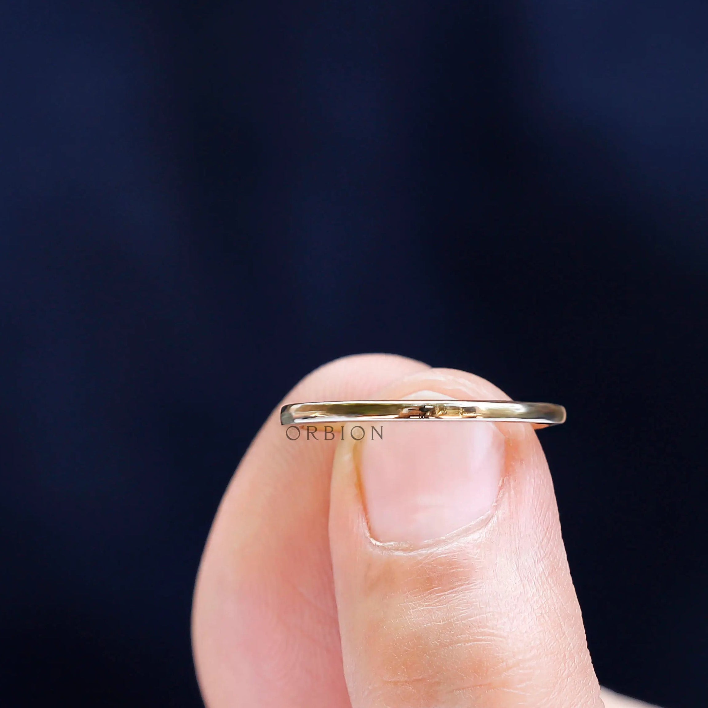Ultra slim polished gold band shown between fingers to highlight fine width