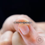 Marquise and round moissanite wedding band held on fingertip, detailed top view