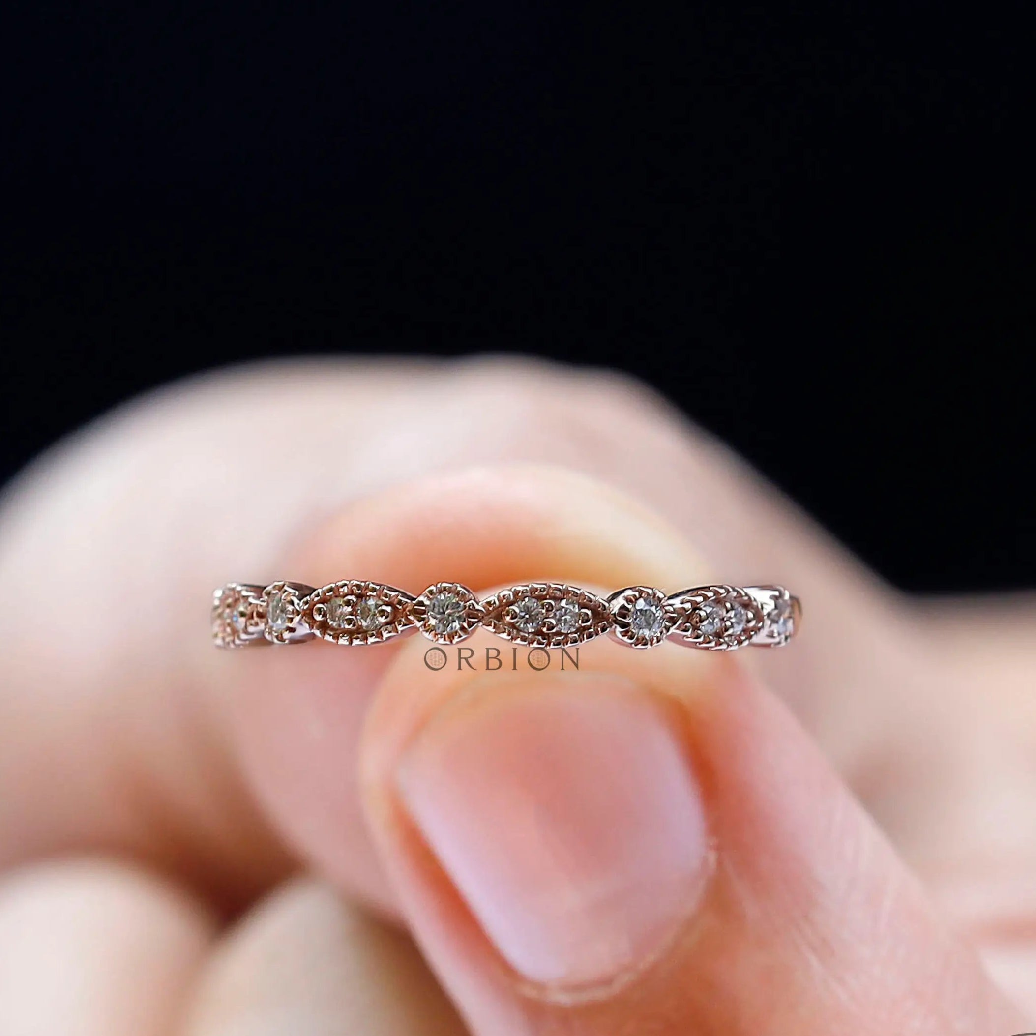 Marquise and round moissanite wedding band held on fingertip, detailed top view
