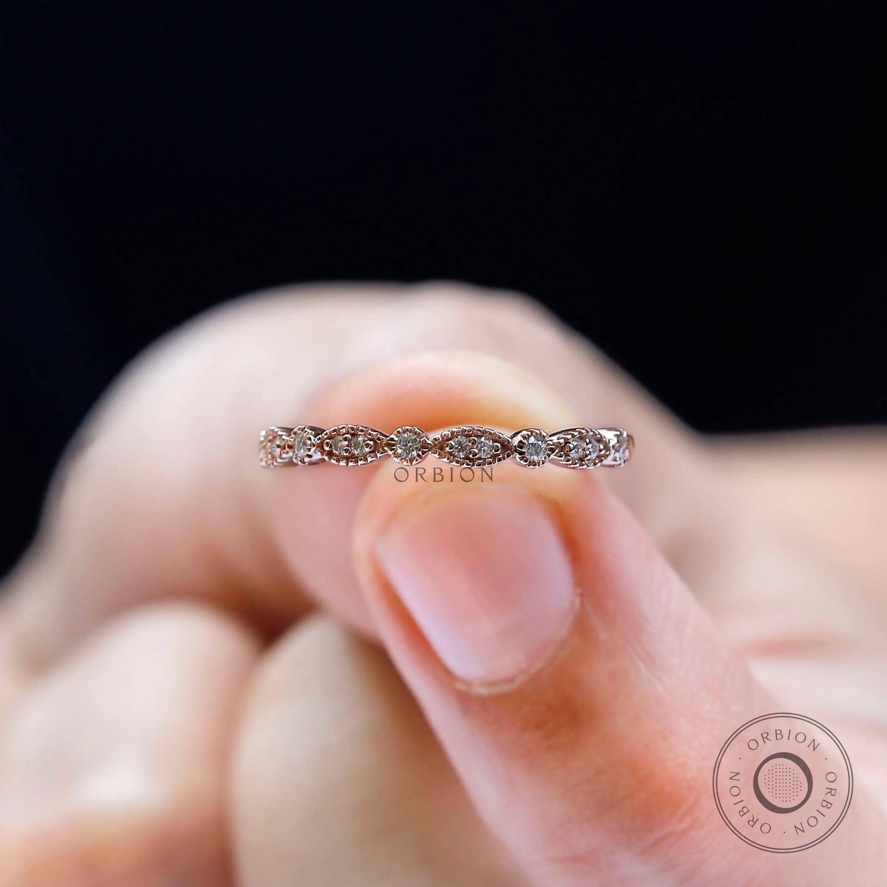 Marquise and round moissanite wedding band held on fingertip, detailed top view
