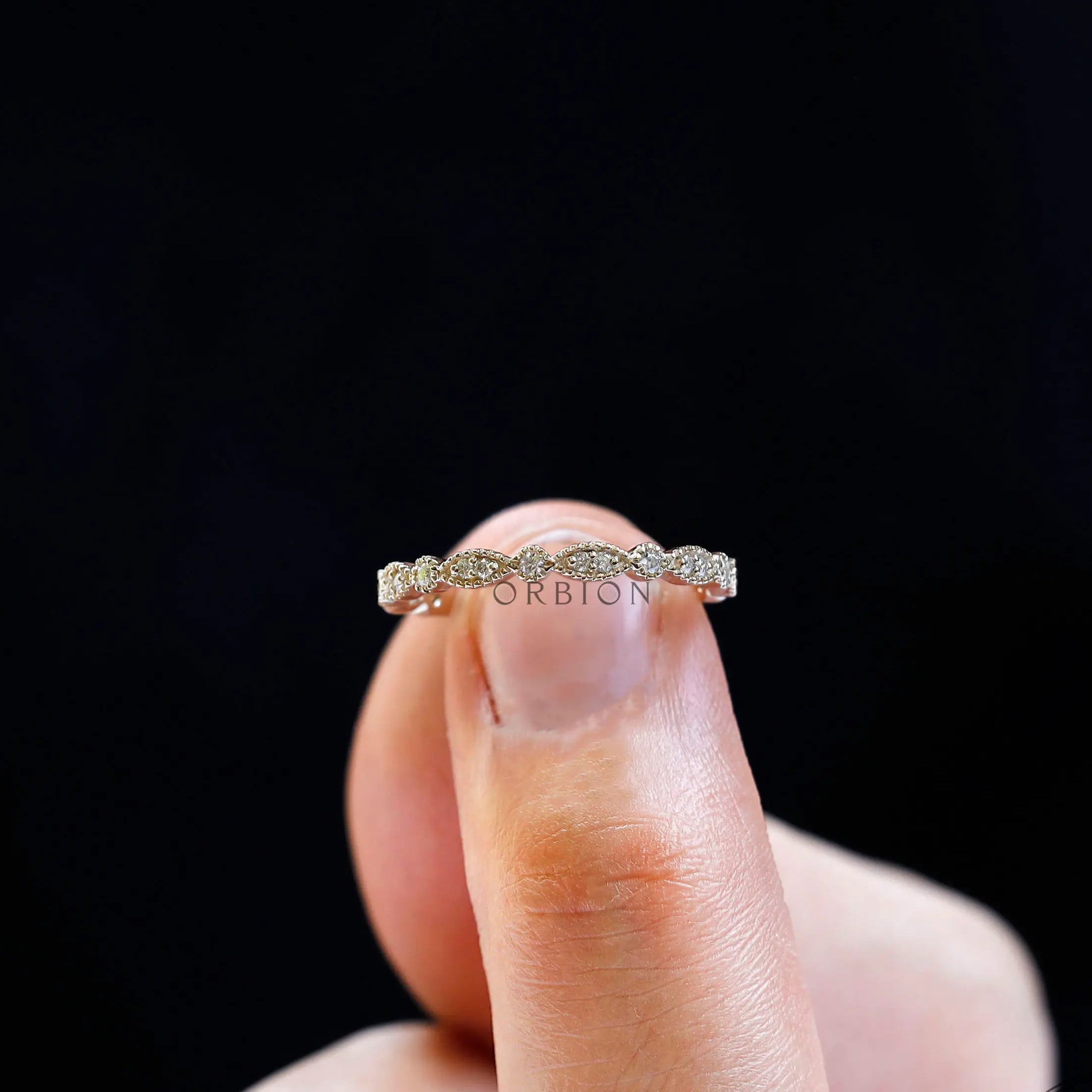 Top view of geometric marquise and round moissanite band held on fingertip