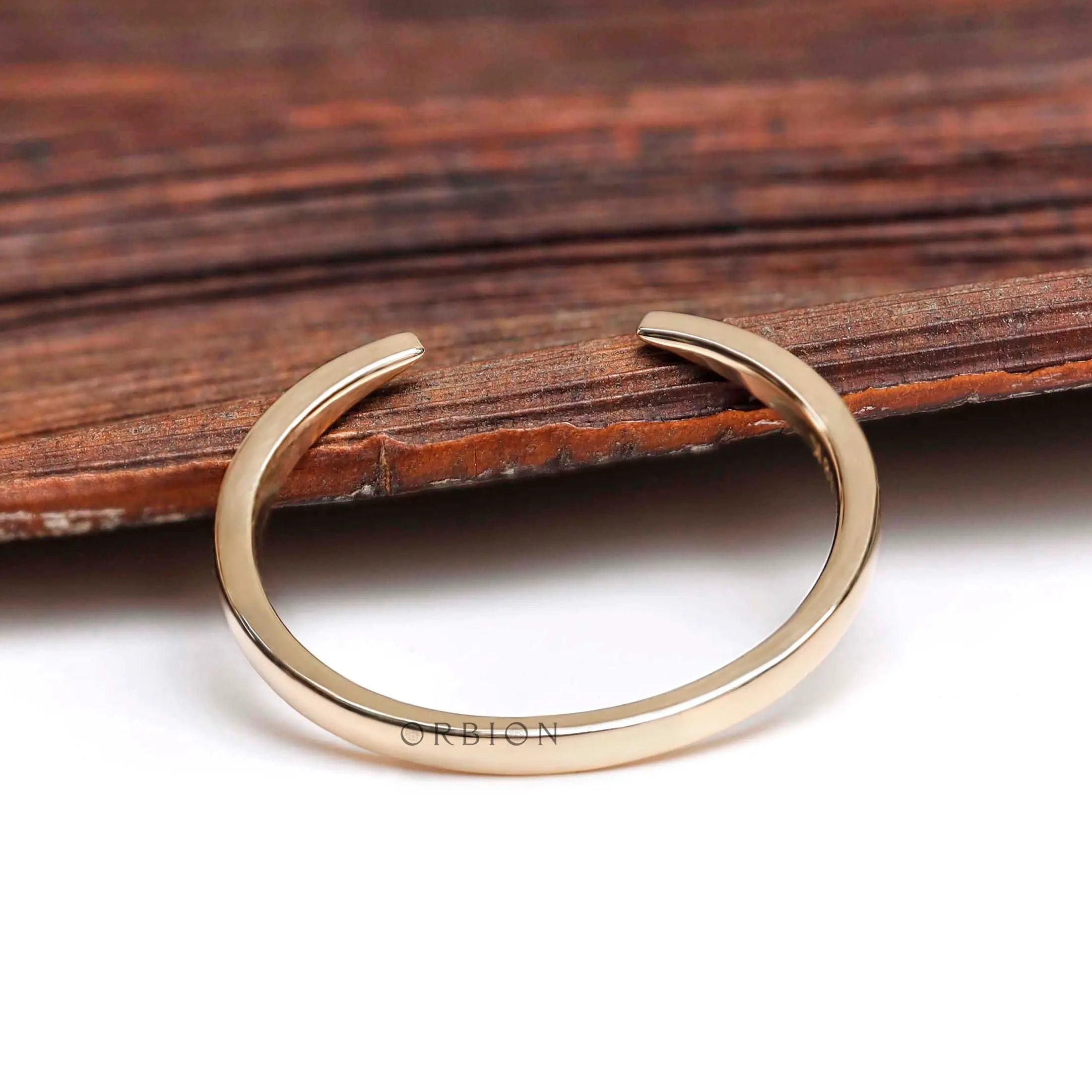 Minimalist open cuff gold wedding band styled on wooden surface