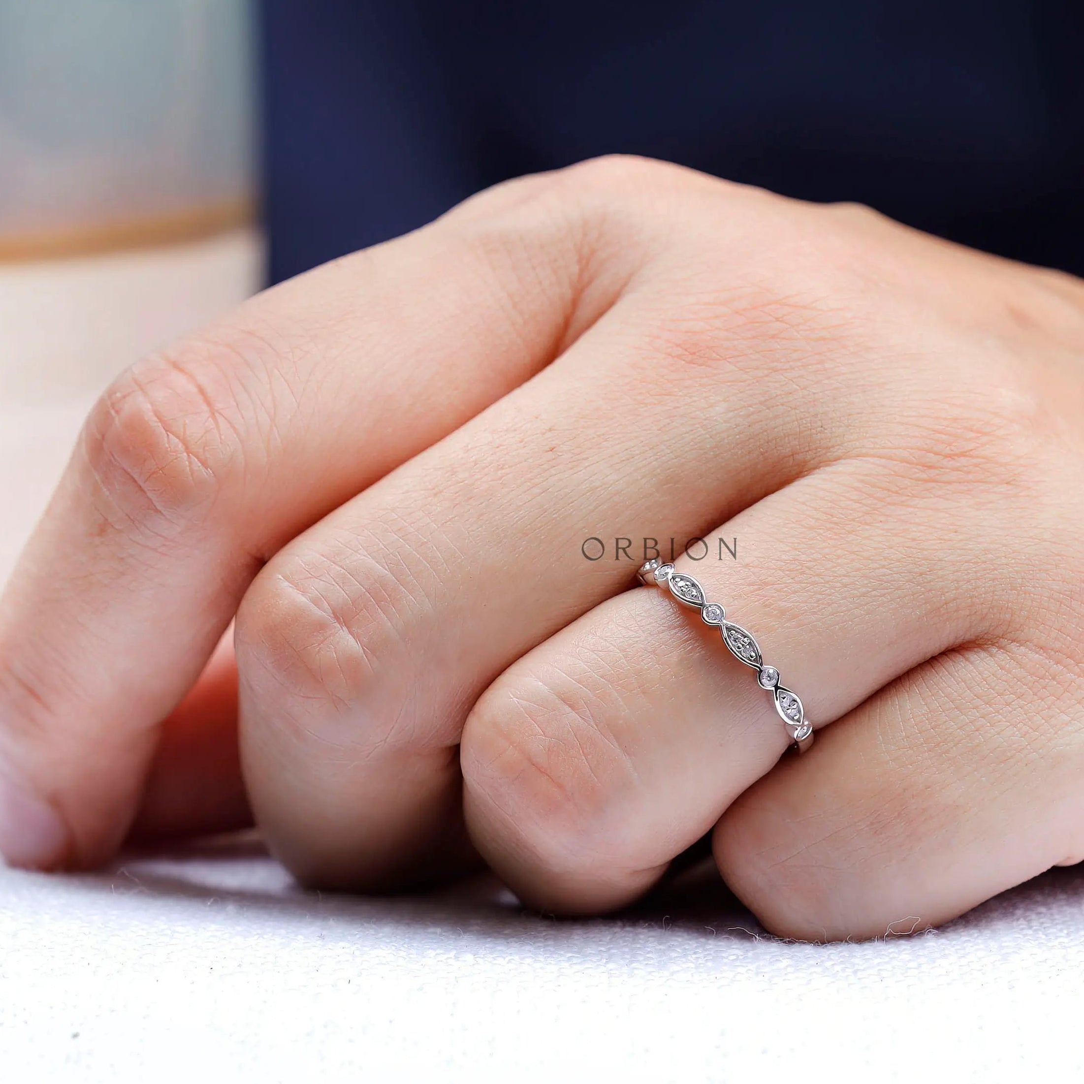 On-hand lifestyle photo of thin Art Deco wedding band with marquise detailing.