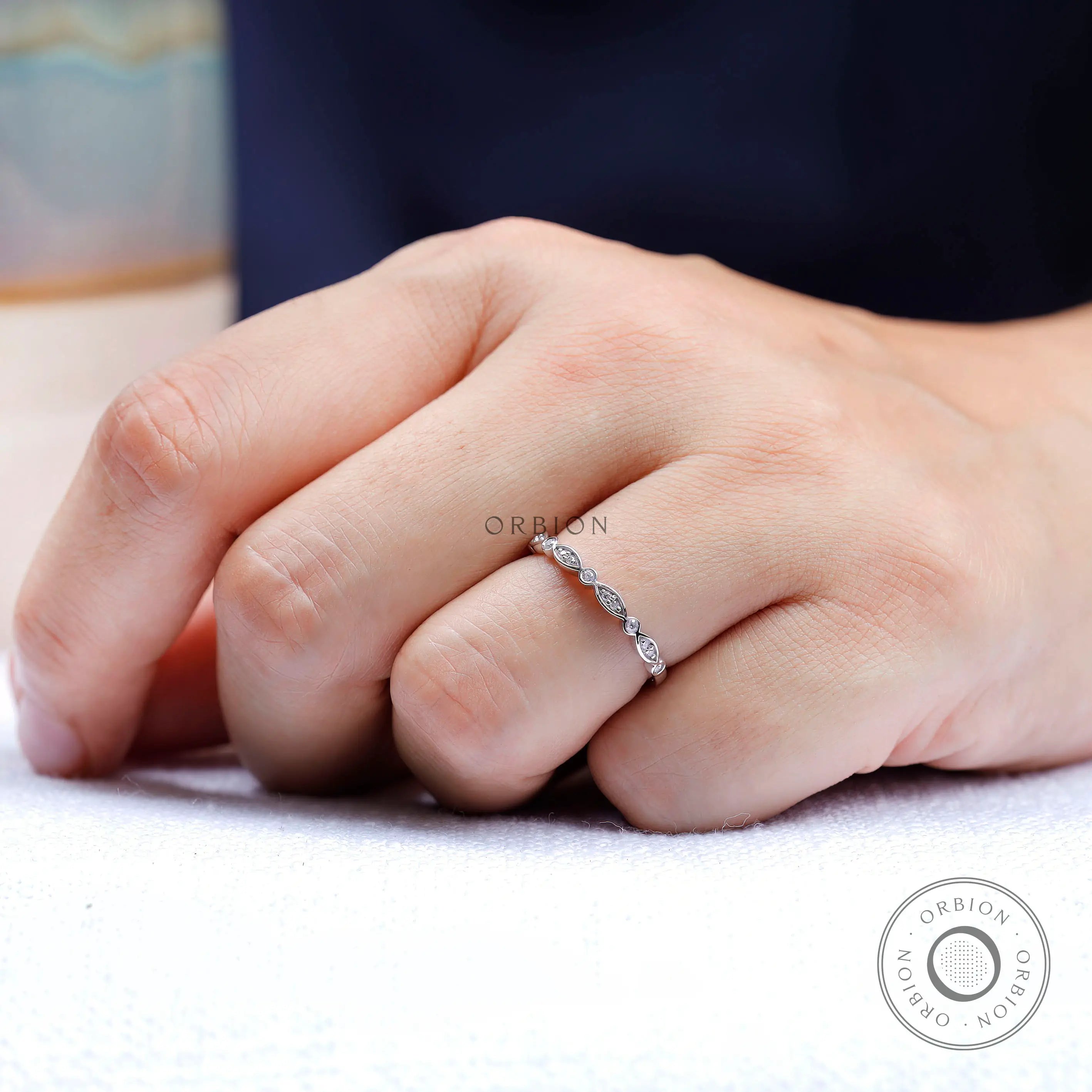 On-hand lifestyle photo of thin Art Deco wedding band with marquise detailing.