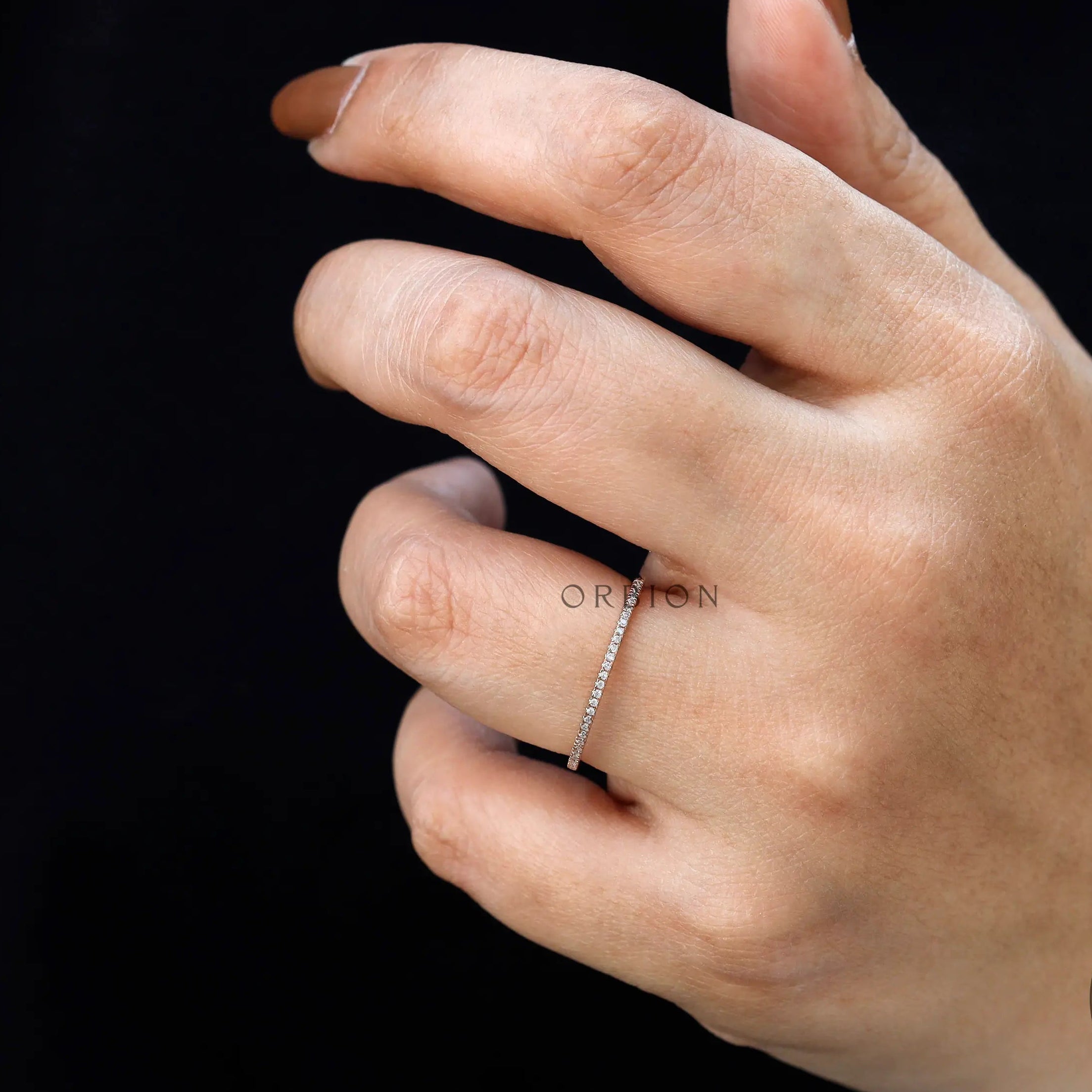 Hand wearing slim pave moissanite stacking ring against black background