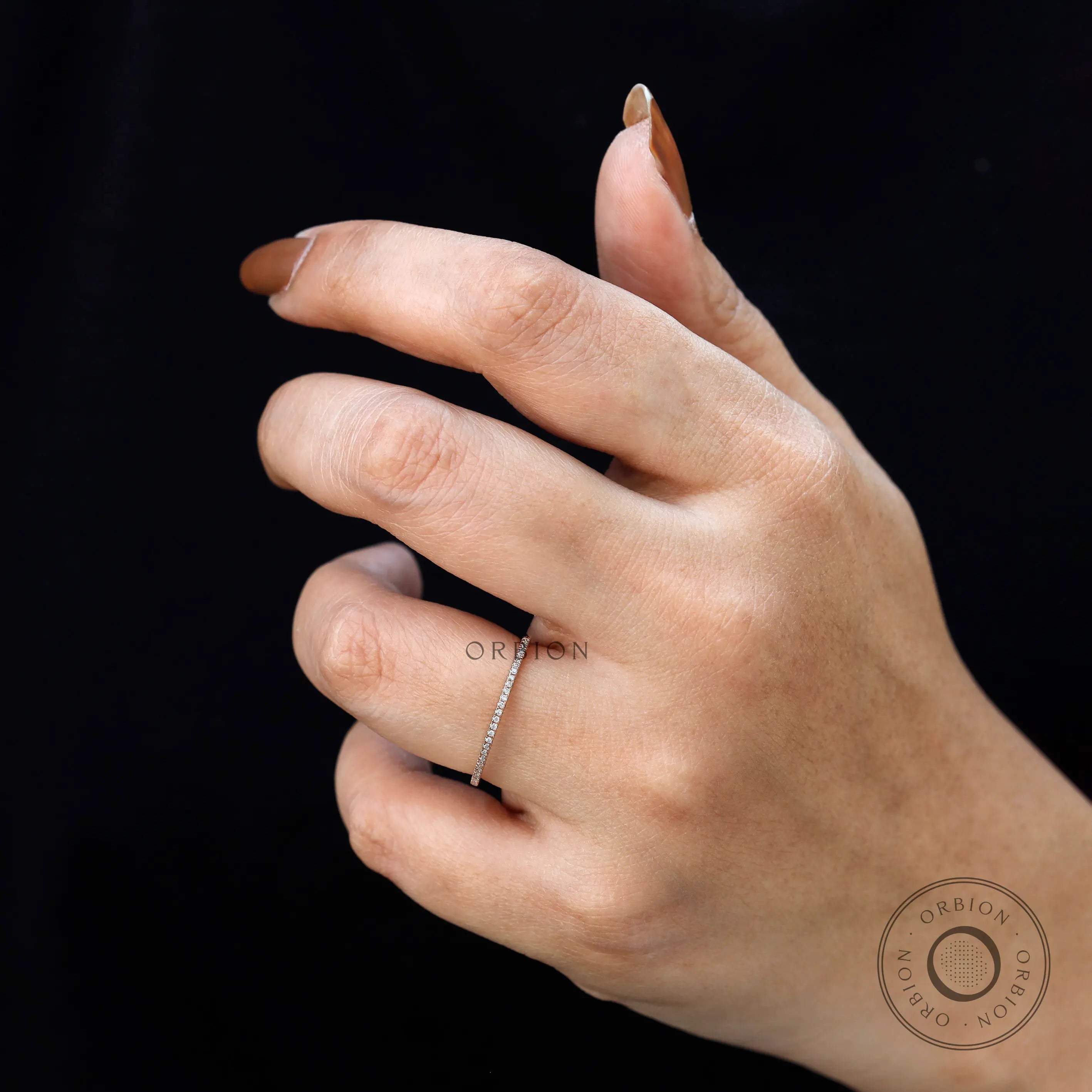 Hand wearing slim pave moissanite stacking ring against black background