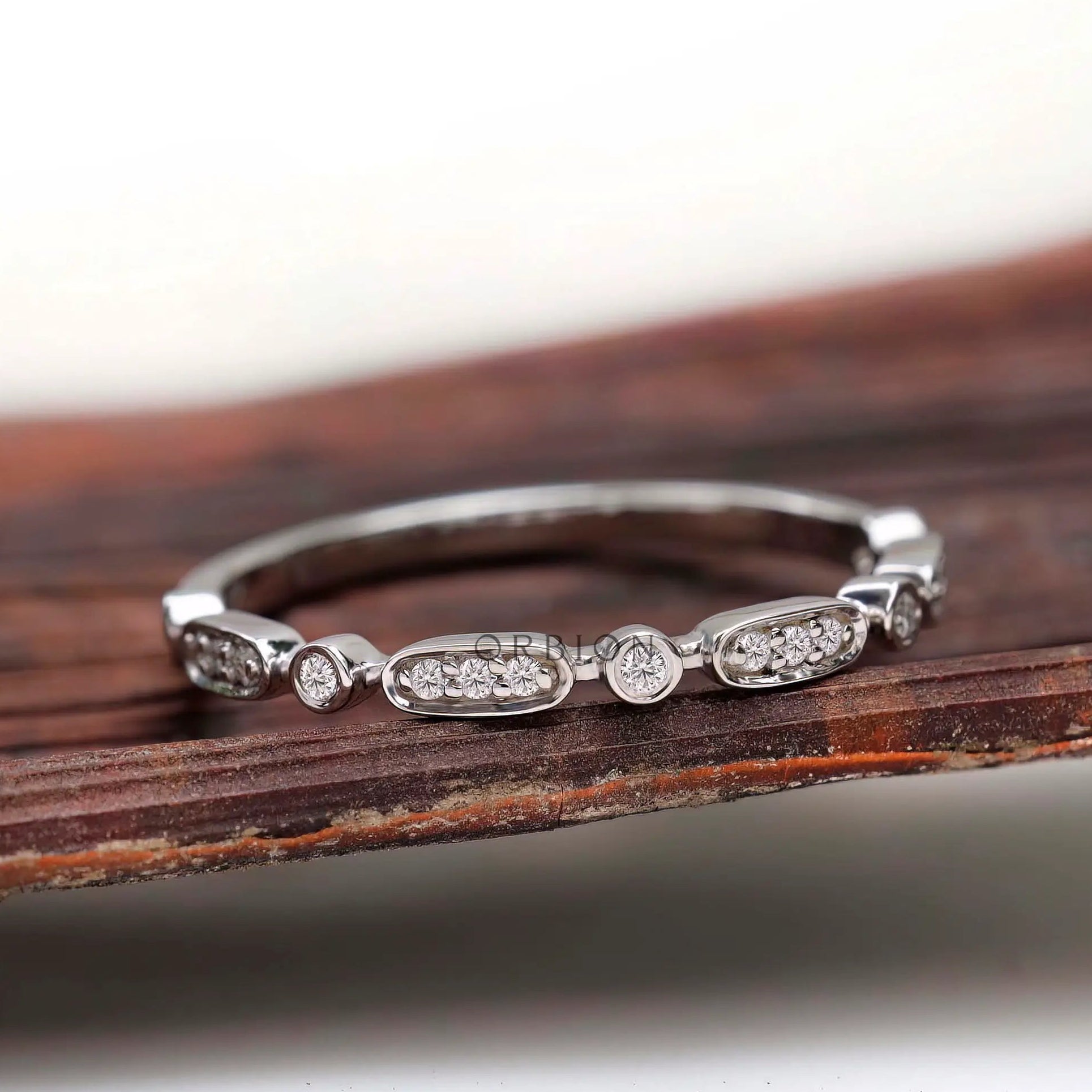Front view of delicate geometric eternity band with oval and bezel-set round accents.