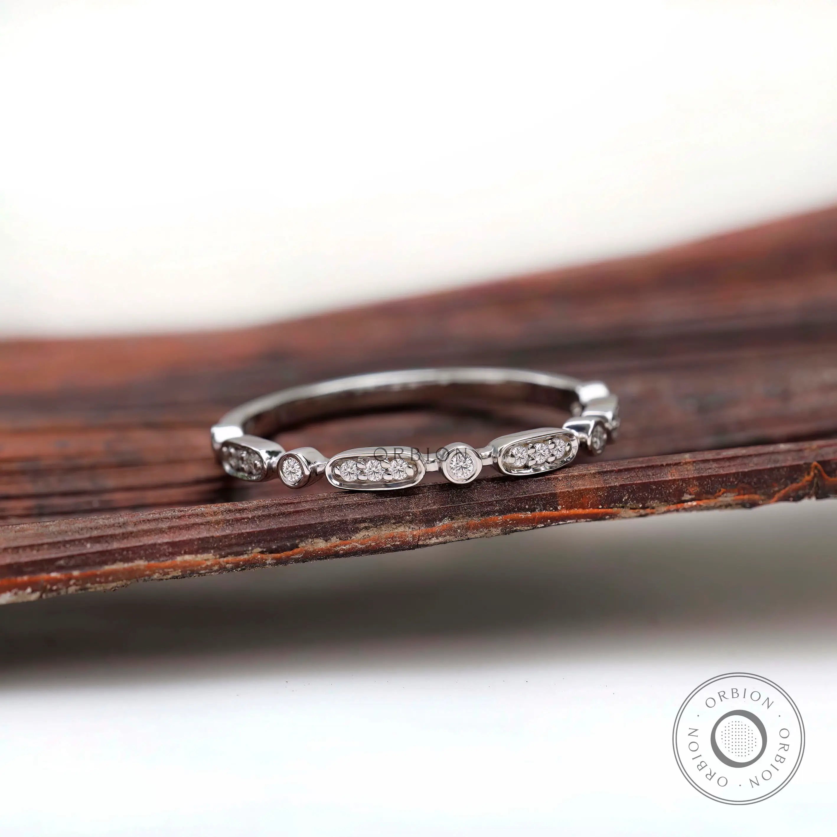 Front view of delicate geometric eternity band with oval and bezel-set round accents.