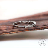 Angled view of slim band showing oval and round bezel accents on a polished shank.