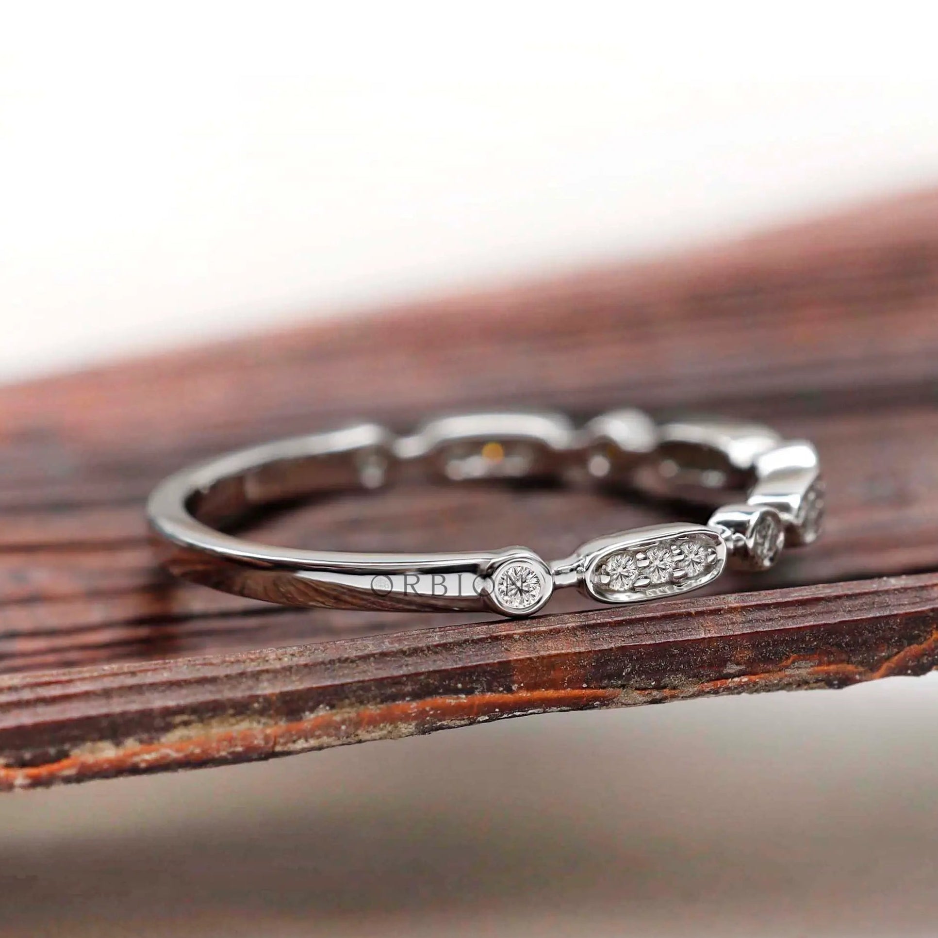 Angled view of slim band showing oval and round bezel accents on a polished shank.