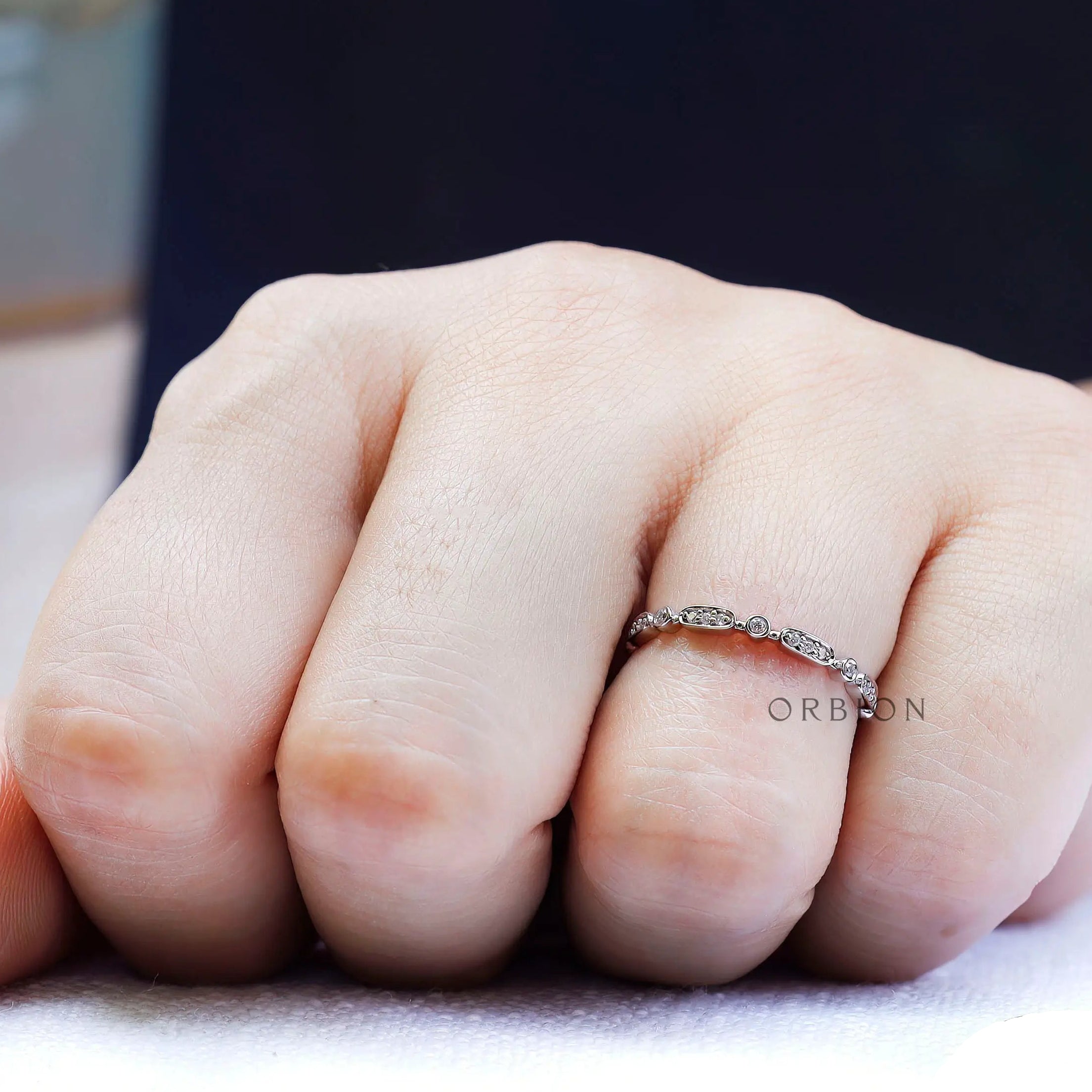 On-hand lifestyle photo of delicate geometric wedding band in a slim stacking style.