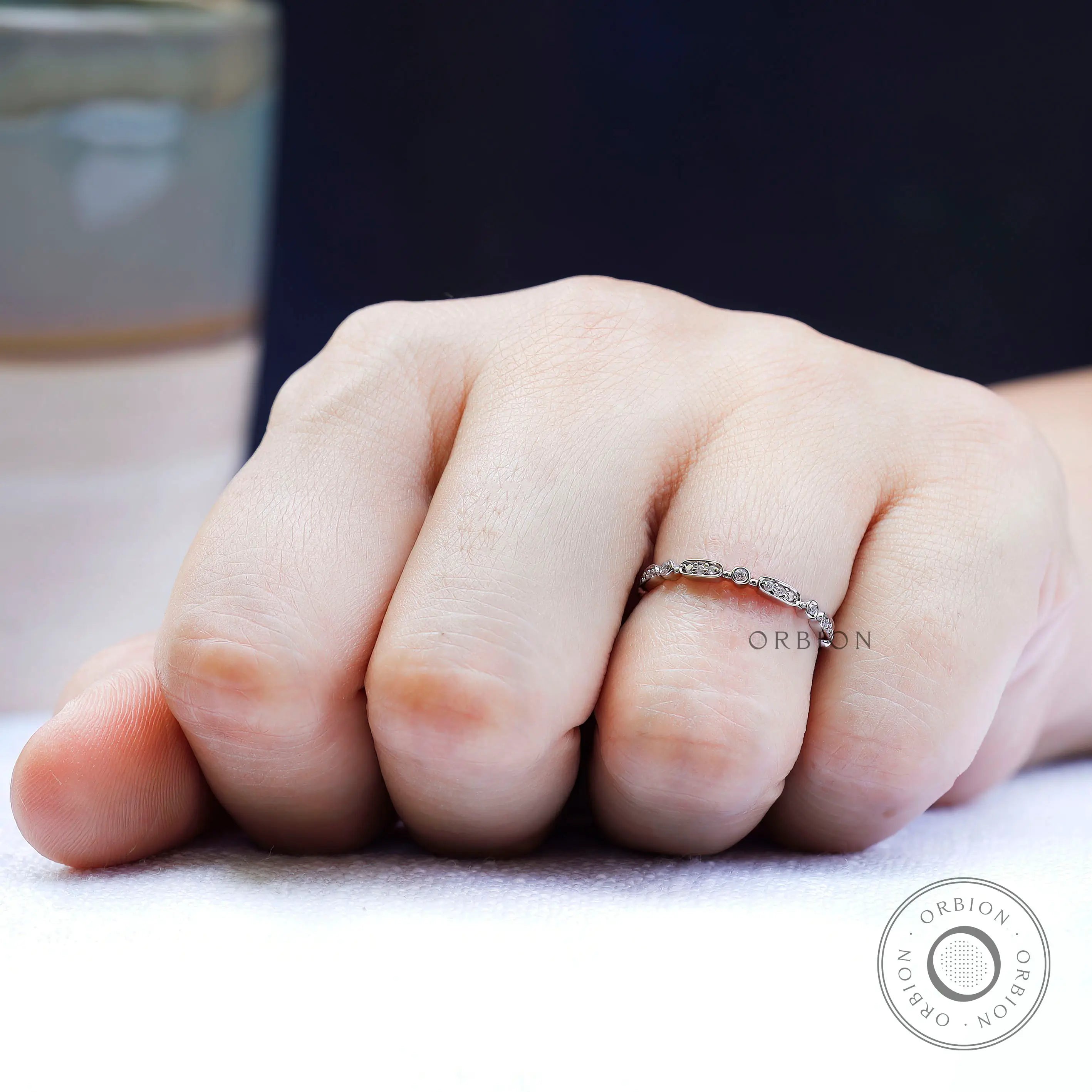 On-hand lifestyle photo of delicate geometric wedding band in a slim stacking style.