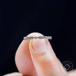 Close-up detail of geometric band held between fingers, showing oval with pave sparkle and round bezel accents.