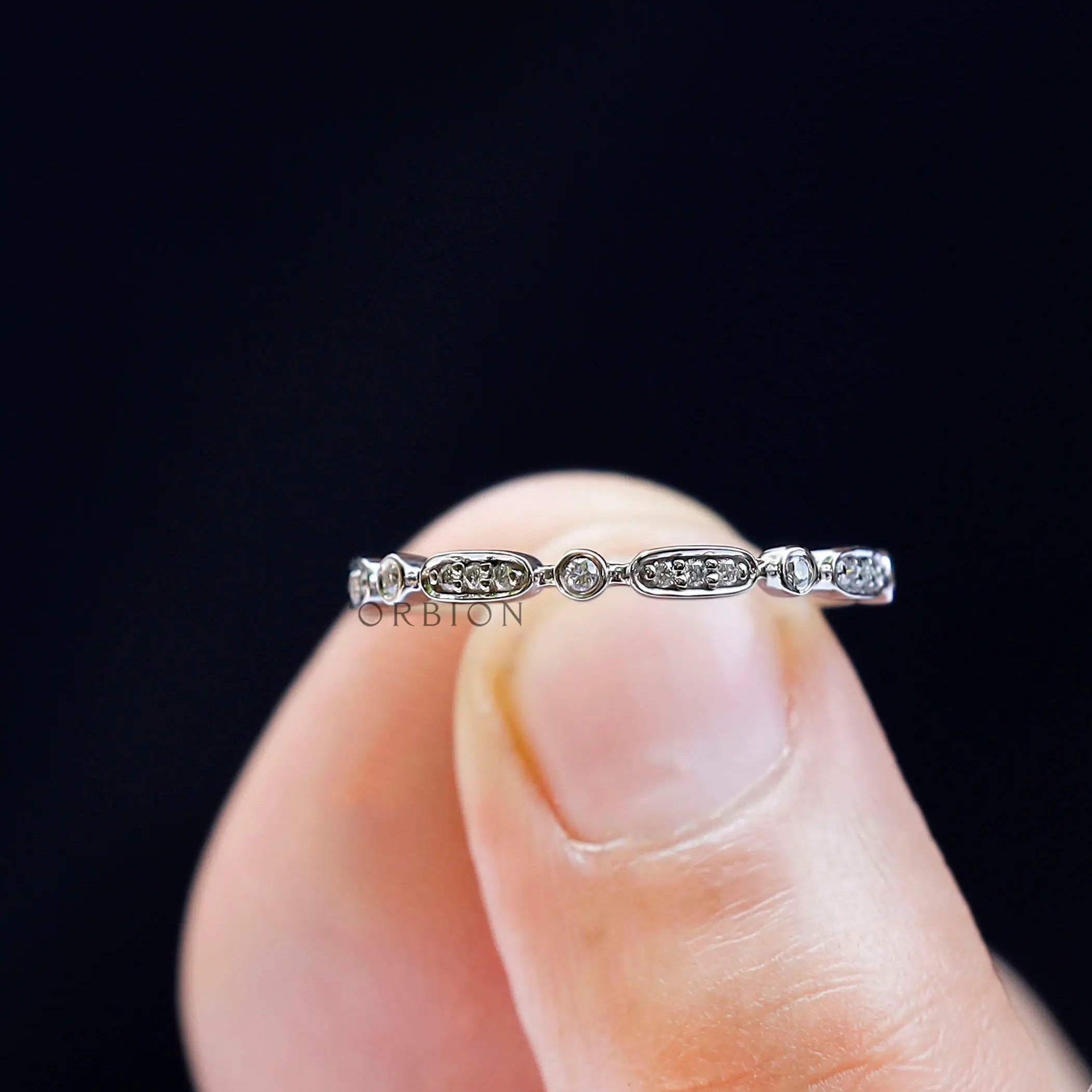 Close-up detail of geometric band held between fingers, showing oval with pave sparkle and round bezel accents.