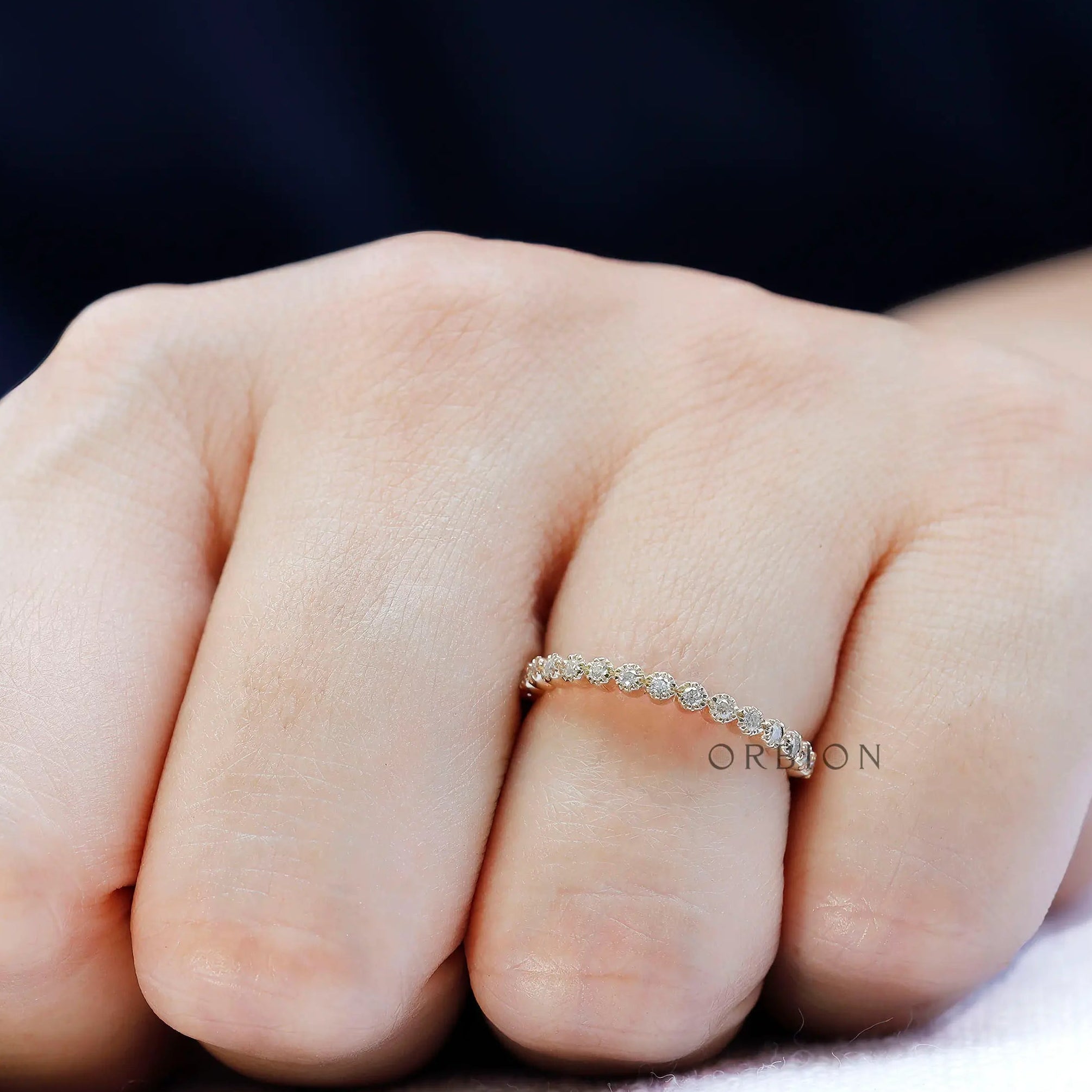 Dainty bezel set moissanite stacking band shown worn on hand