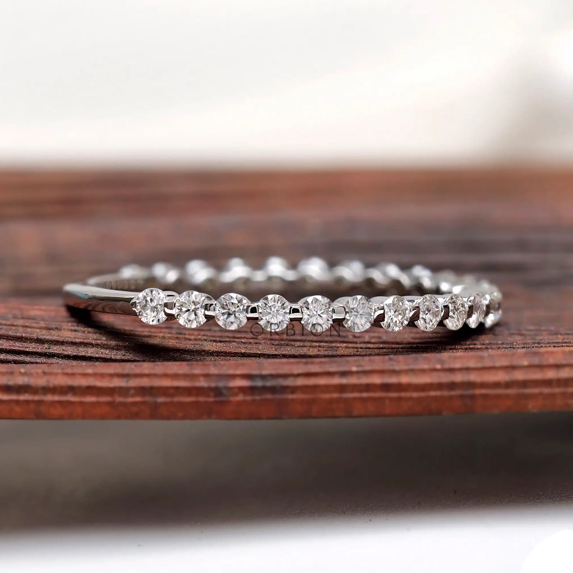 Shared prong round moissanite eternity wedding band angled side view on wood