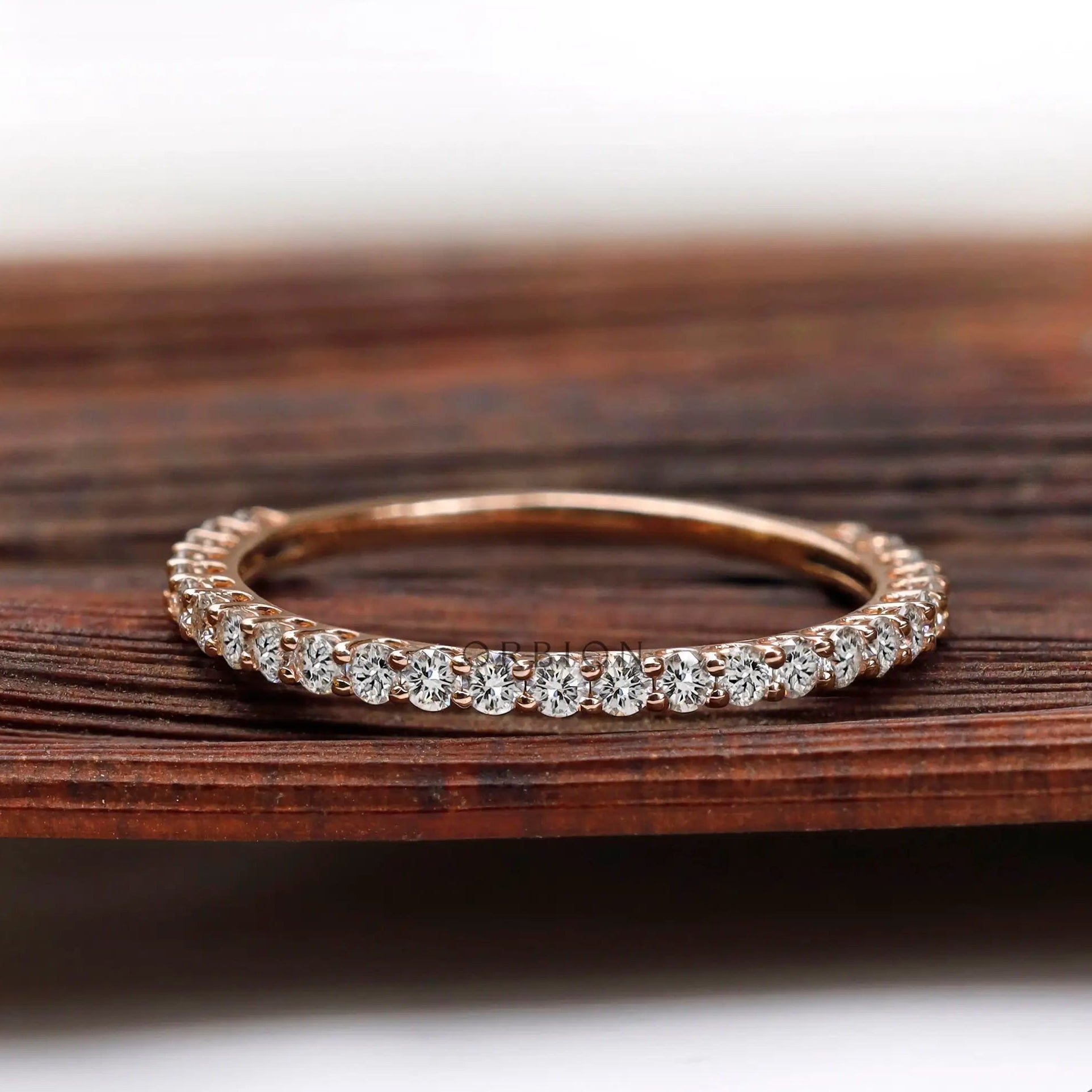 U-prong round eternity band in rose gold shown from front on wood backdrop