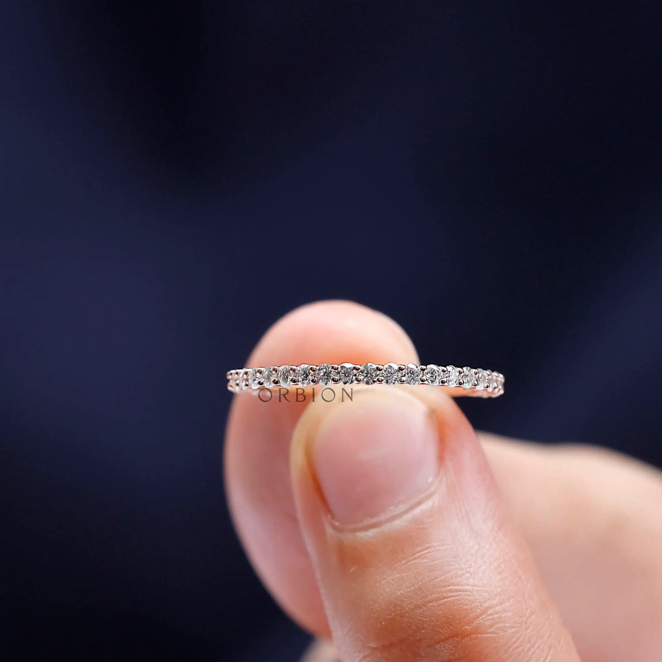Close-up of U-prong round eternity band in rose gold held between fingers