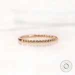 Angled side view of gold beaded wedding band highlighting slim profile