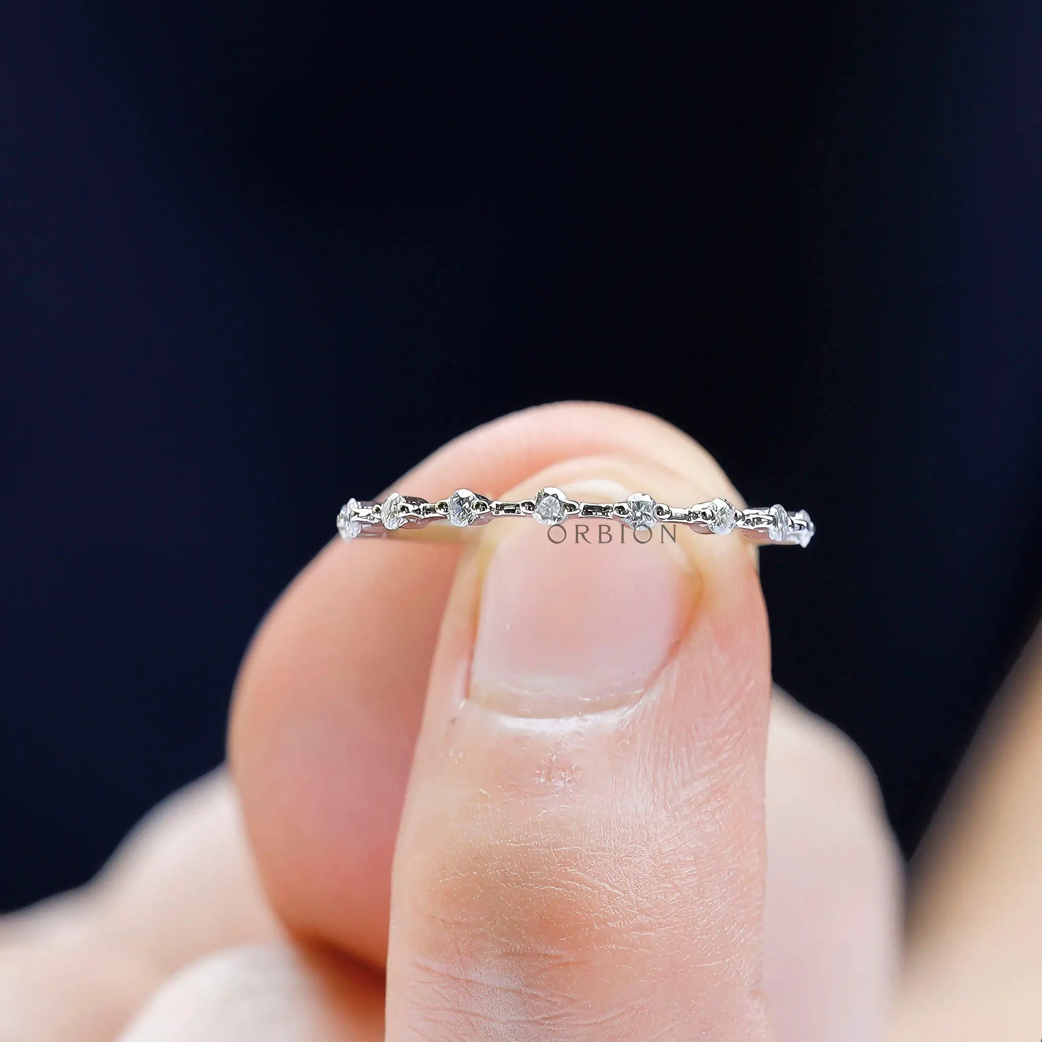 Worn fingertip view of delicate diamond beaded eternity band in white gold.