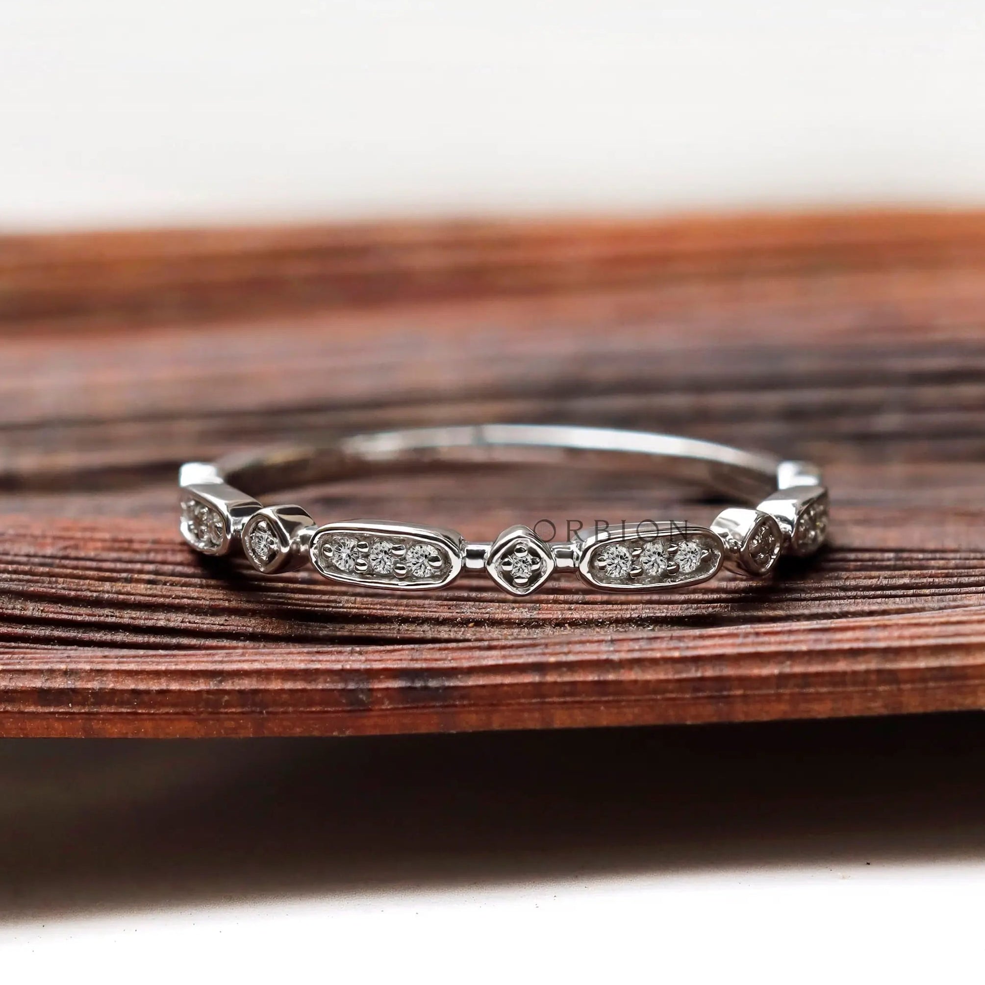 Dainty geometric moissanite wedding band displayed on wooden surface front view