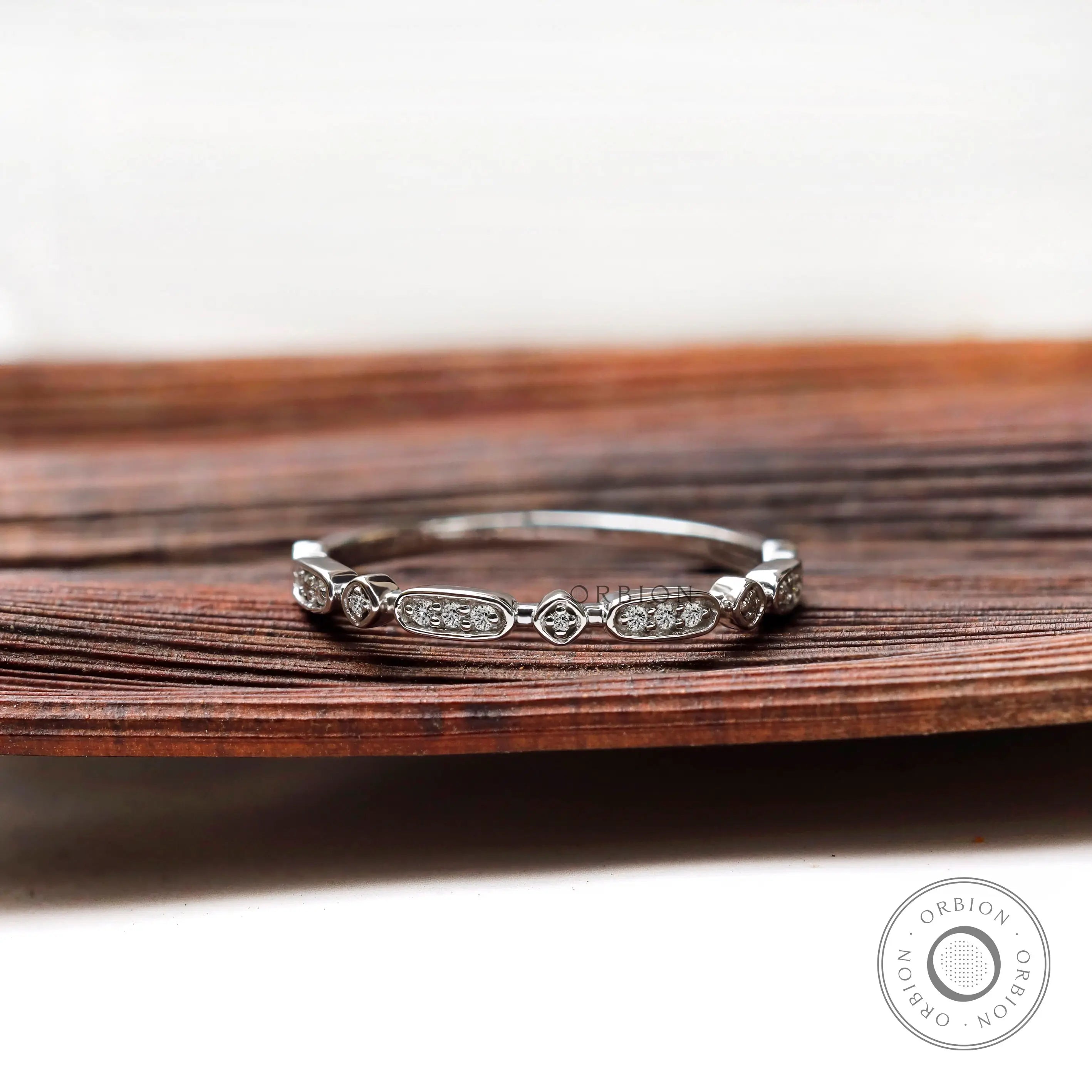 Dainty geometric moissanite wedding band displayed on wooden surface front view