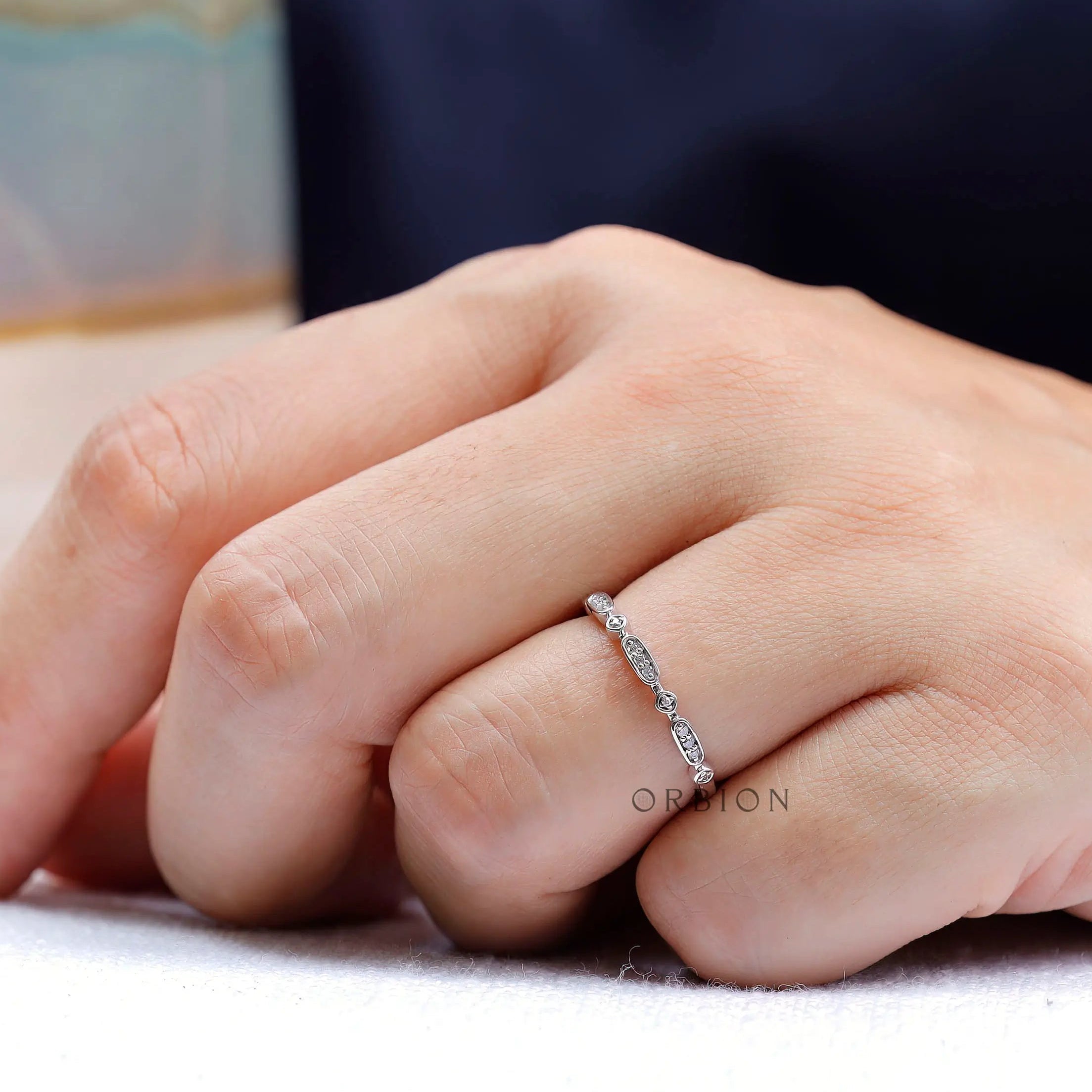 Dainty geometric moissanite wedding band worn on finger close-up